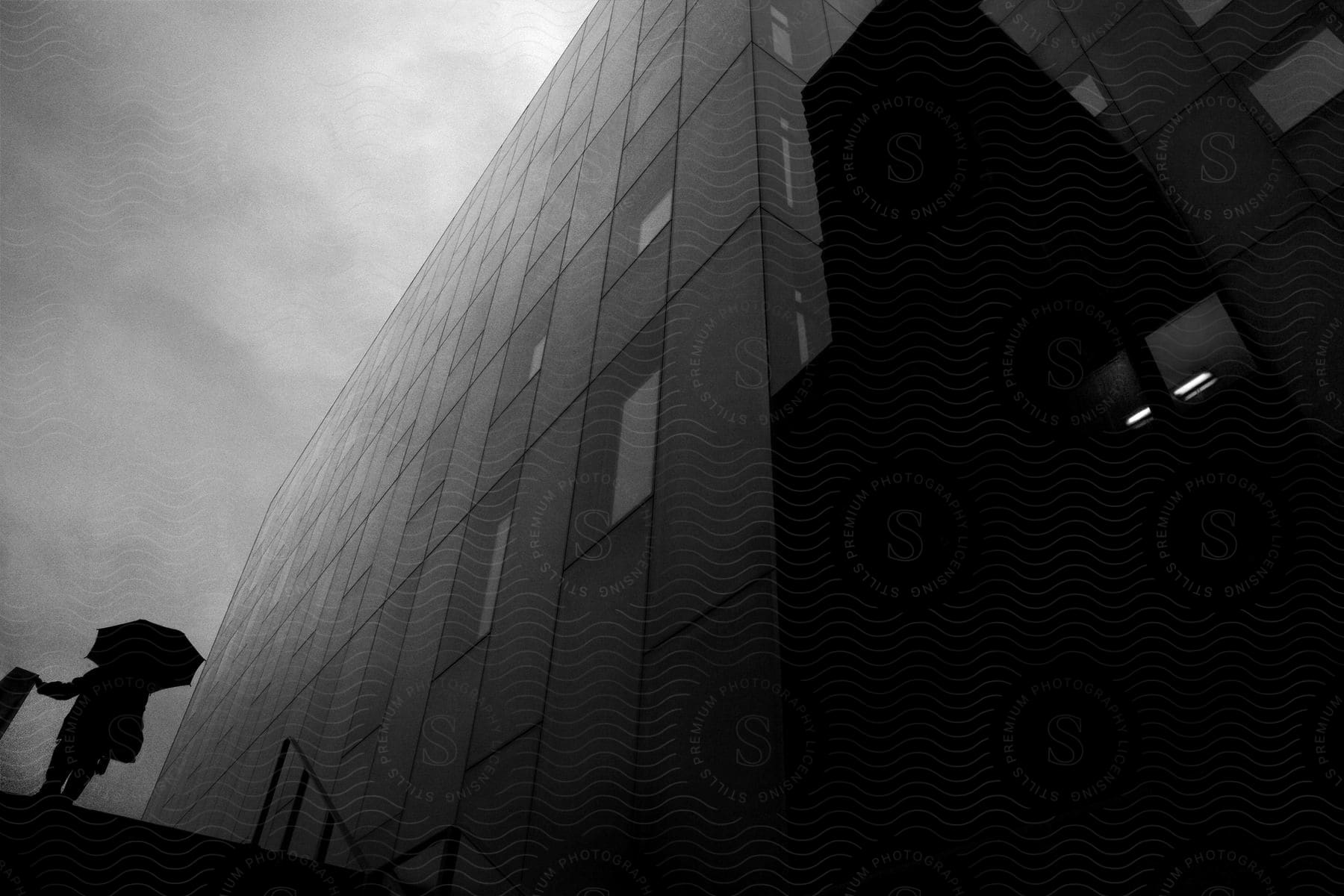 A person walks in front of a tall black and white building with an umbrella