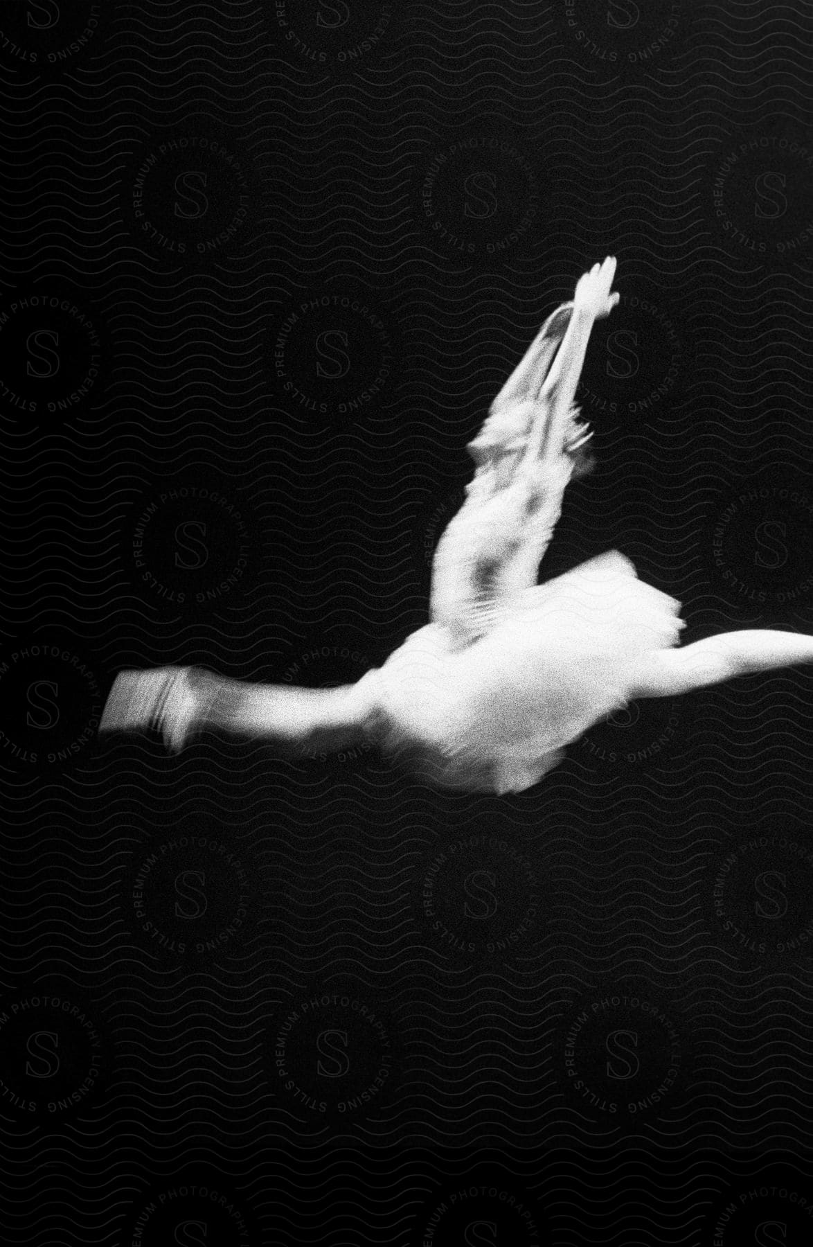 A ballerina in midair with arms and legs extended against a black background