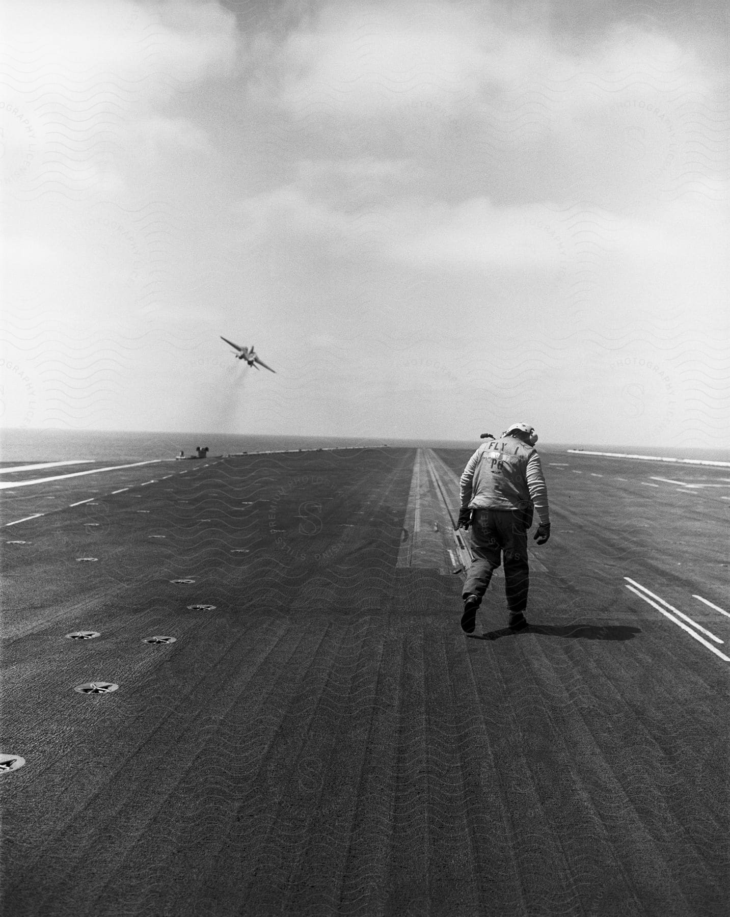 A person standing on a runway on a boat with an airplane flying nearby