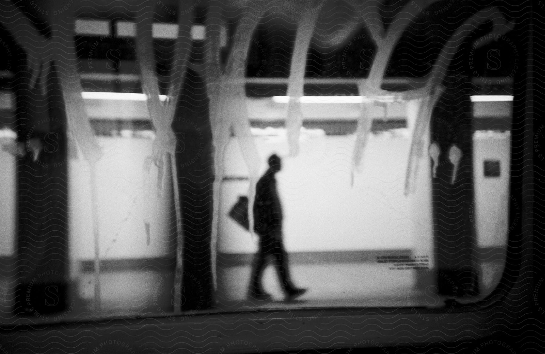 A blurry black and white silhouette of a man walking on a subway platform seen from inside the train with painted letters on the window