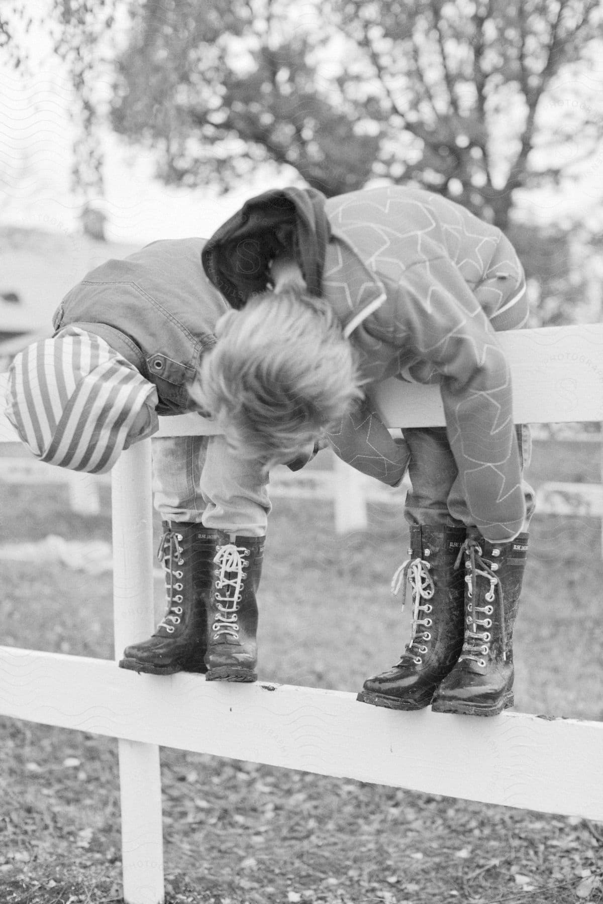 Two children in winter clothing lean over a fence they have climbed