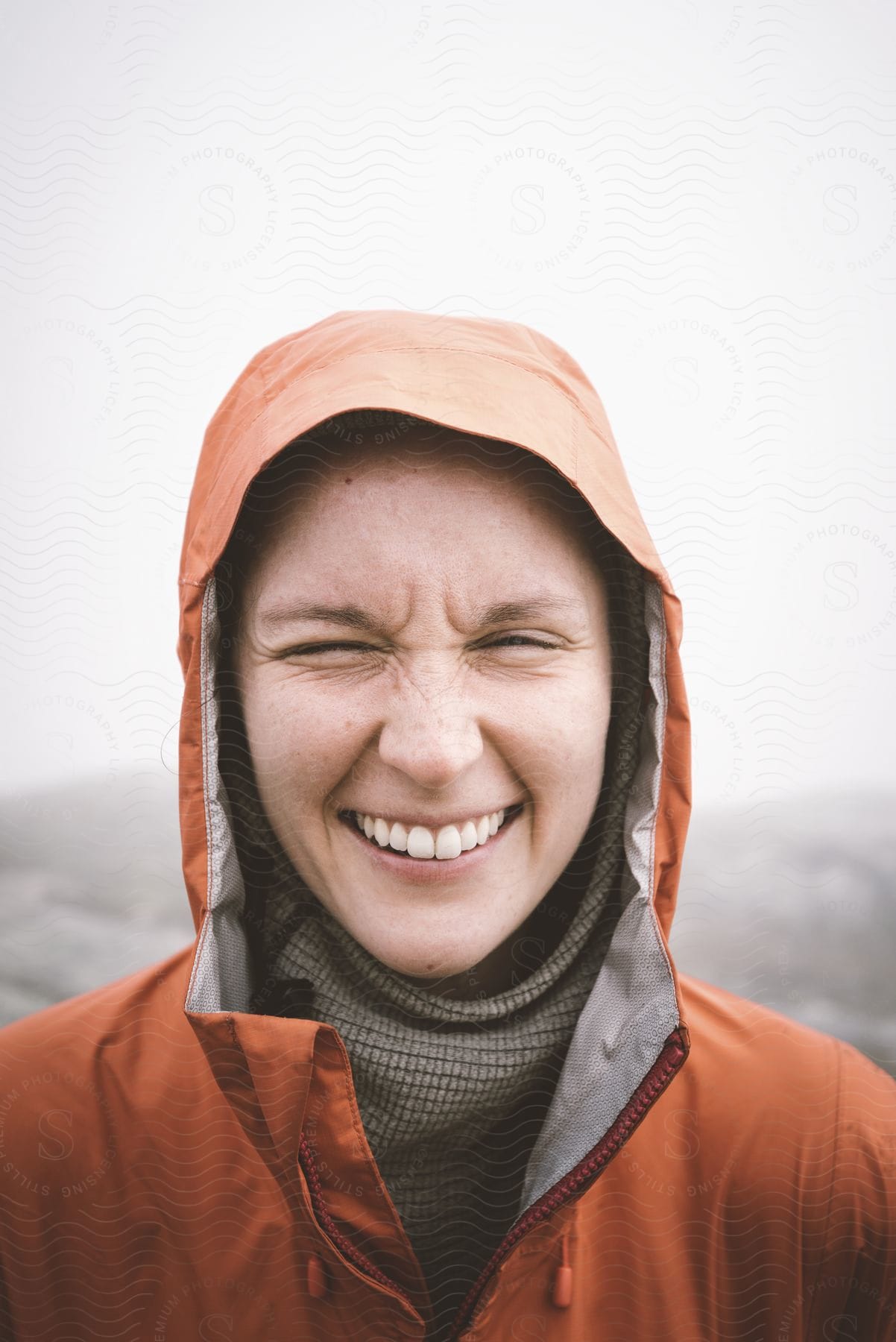 A woman wearing a jacket and a hood with a wide smile on her face