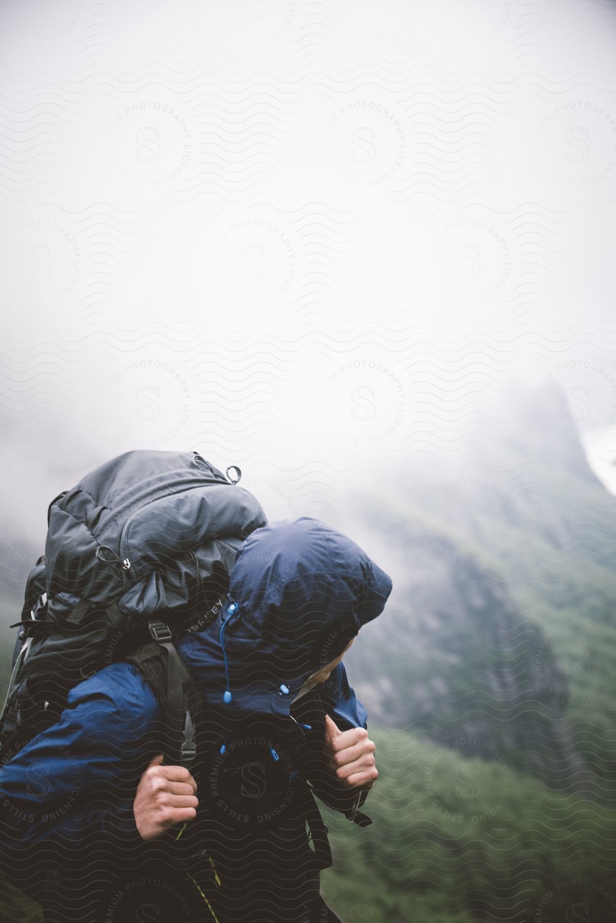 A man wearing mountaineering equipment and a backpack looks down the mountain slopes