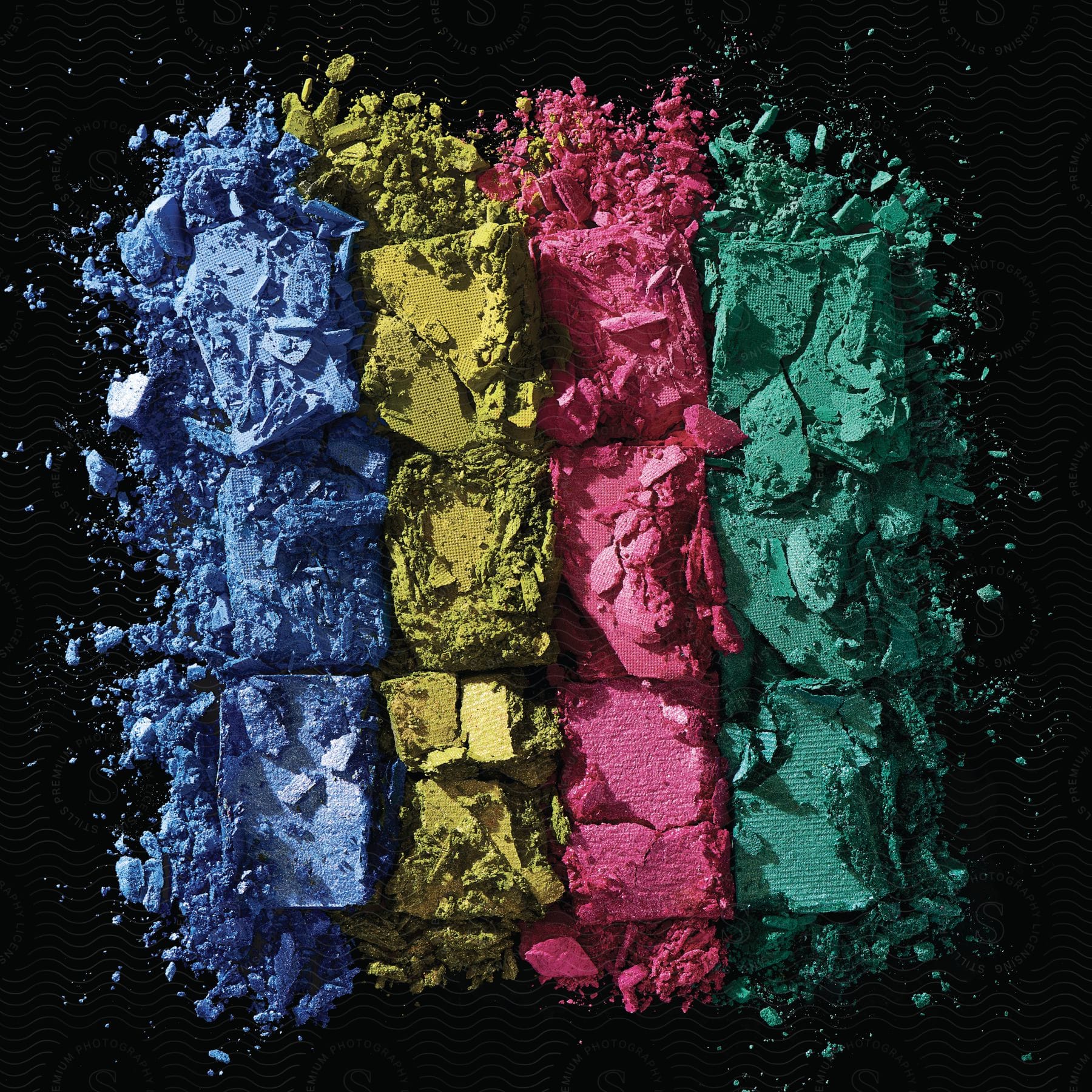 Stock photo of crushed eyeshadow squares in four colors arranged in vertical rows against a black background