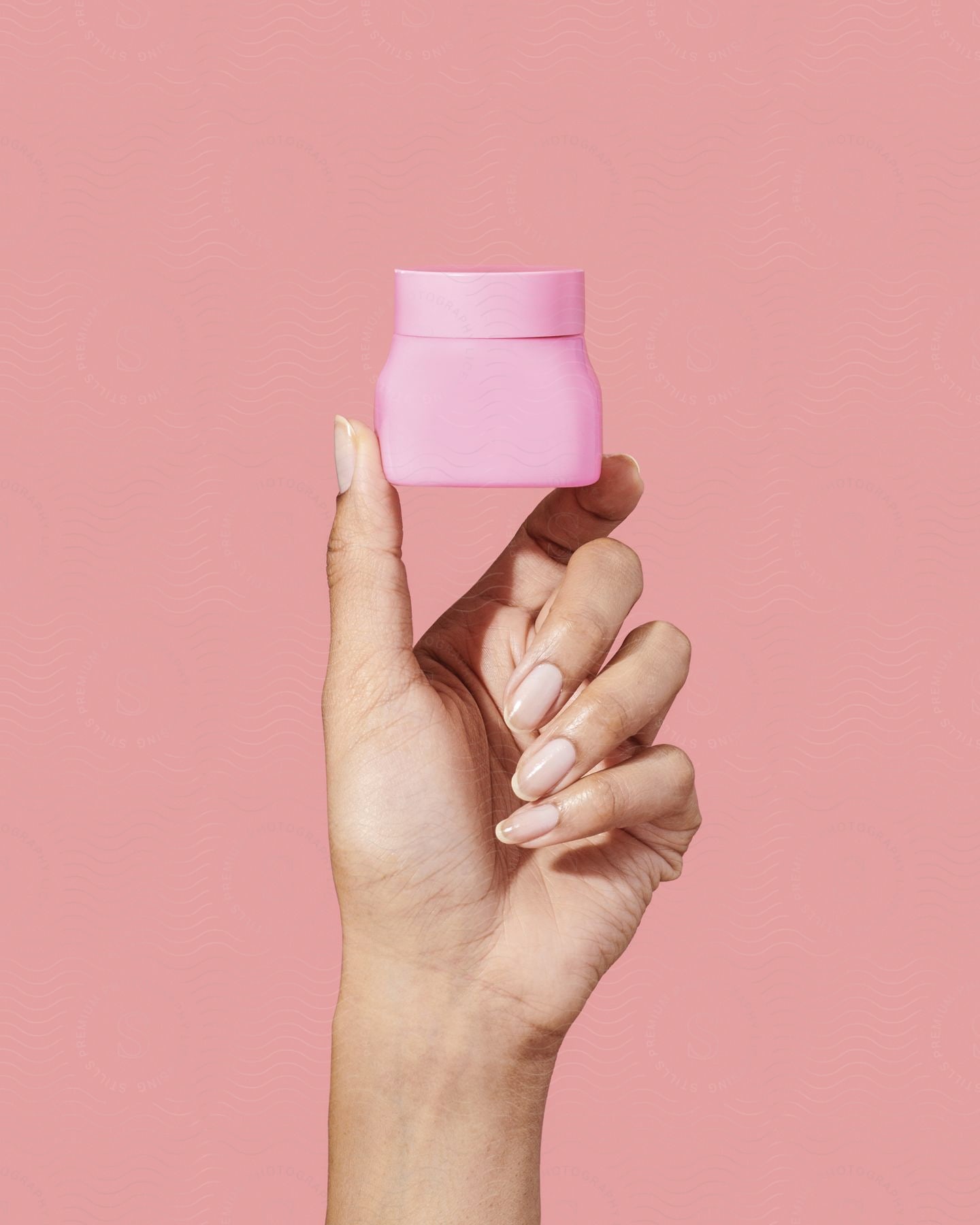 A female hand displaying a pink cosmetic product