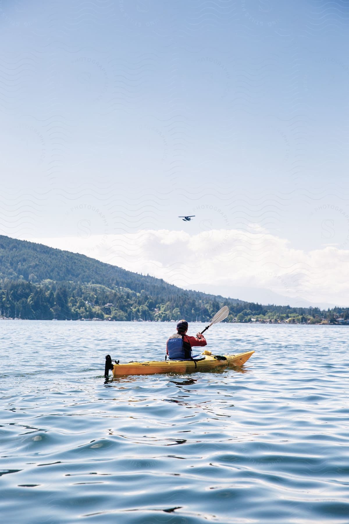 A man paddling a canoe in calm water with a hill in the background