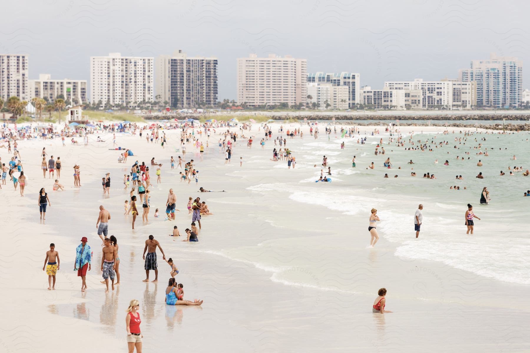 A large crowd of people enjoying the beach and cityscape