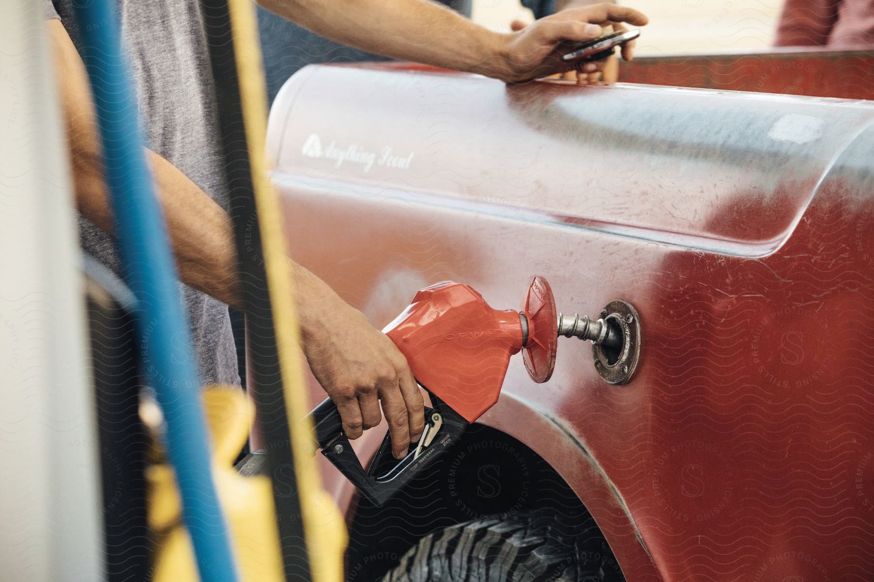 A person wearing a gray tshirt is filling up a red pickup truck