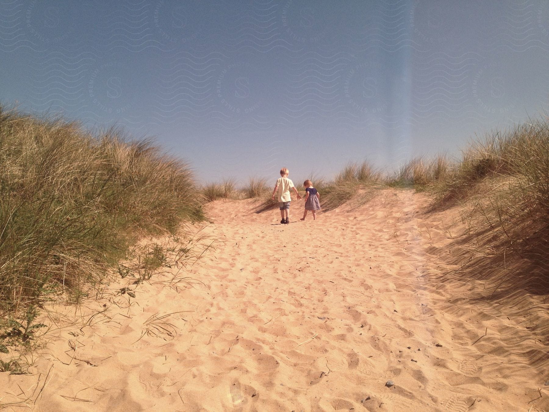 Two children a boy and a girl walk on a grassy plain with sand