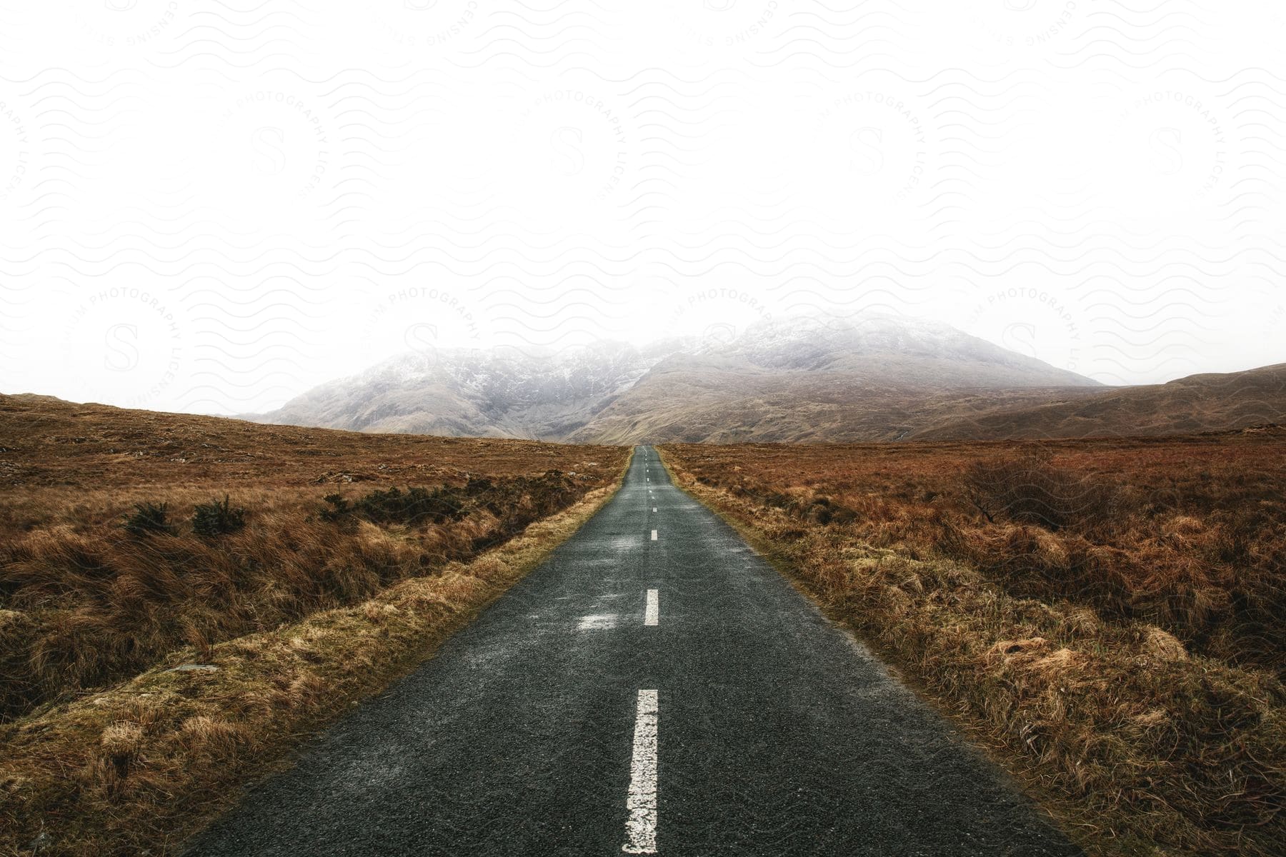 A road stretches through the countryside towards a fogcovered hill