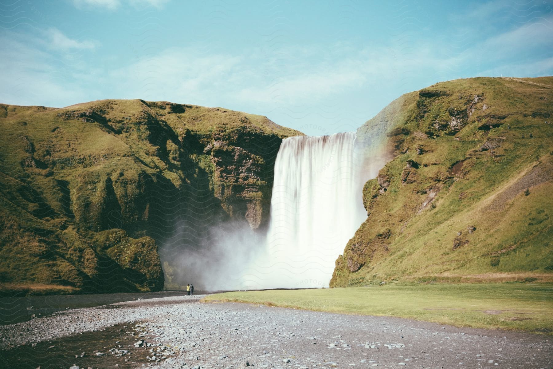 People near river at base of waterfall on cloudy day