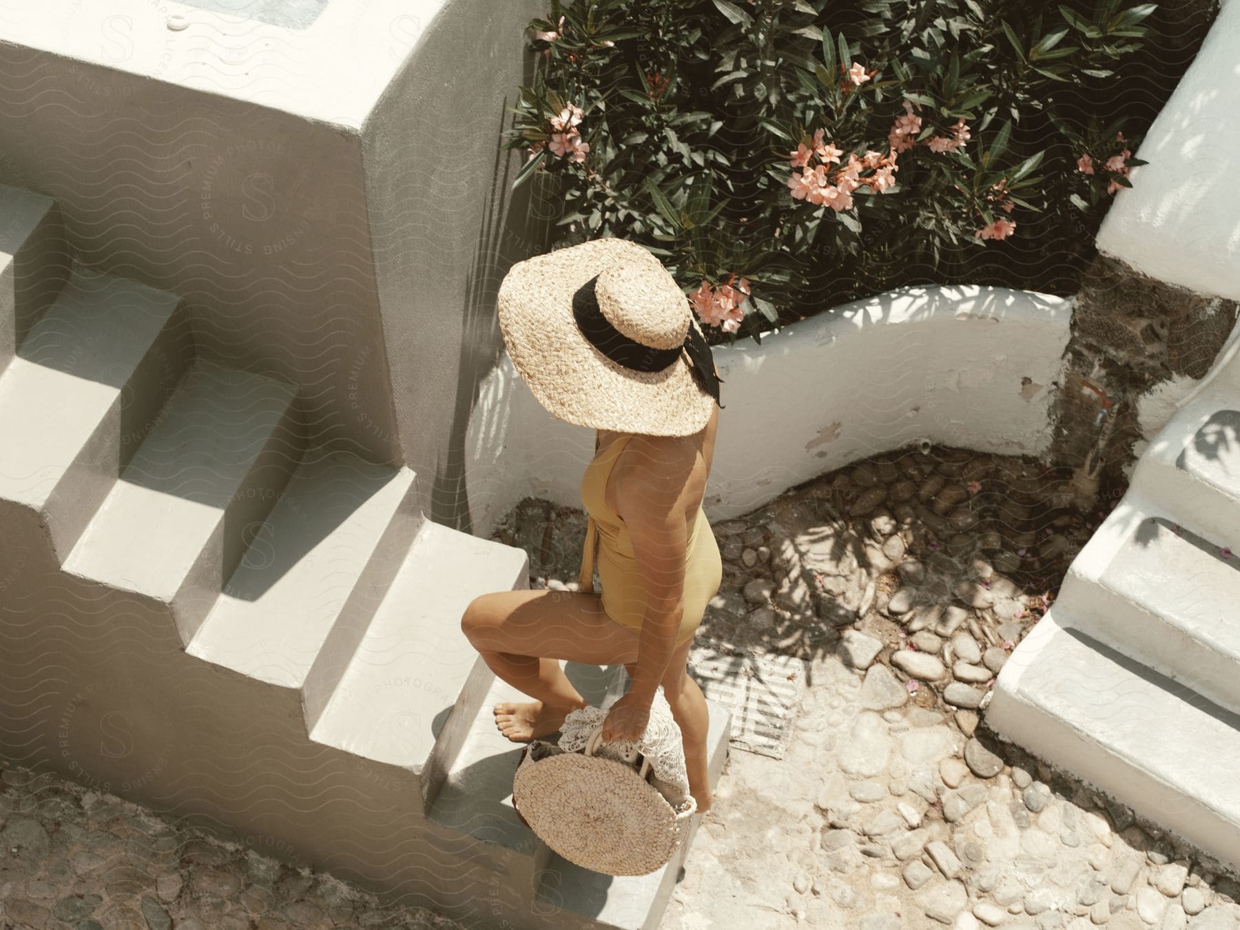 A woman wearing a bathing suit and sun hat is walking up steps to a villa