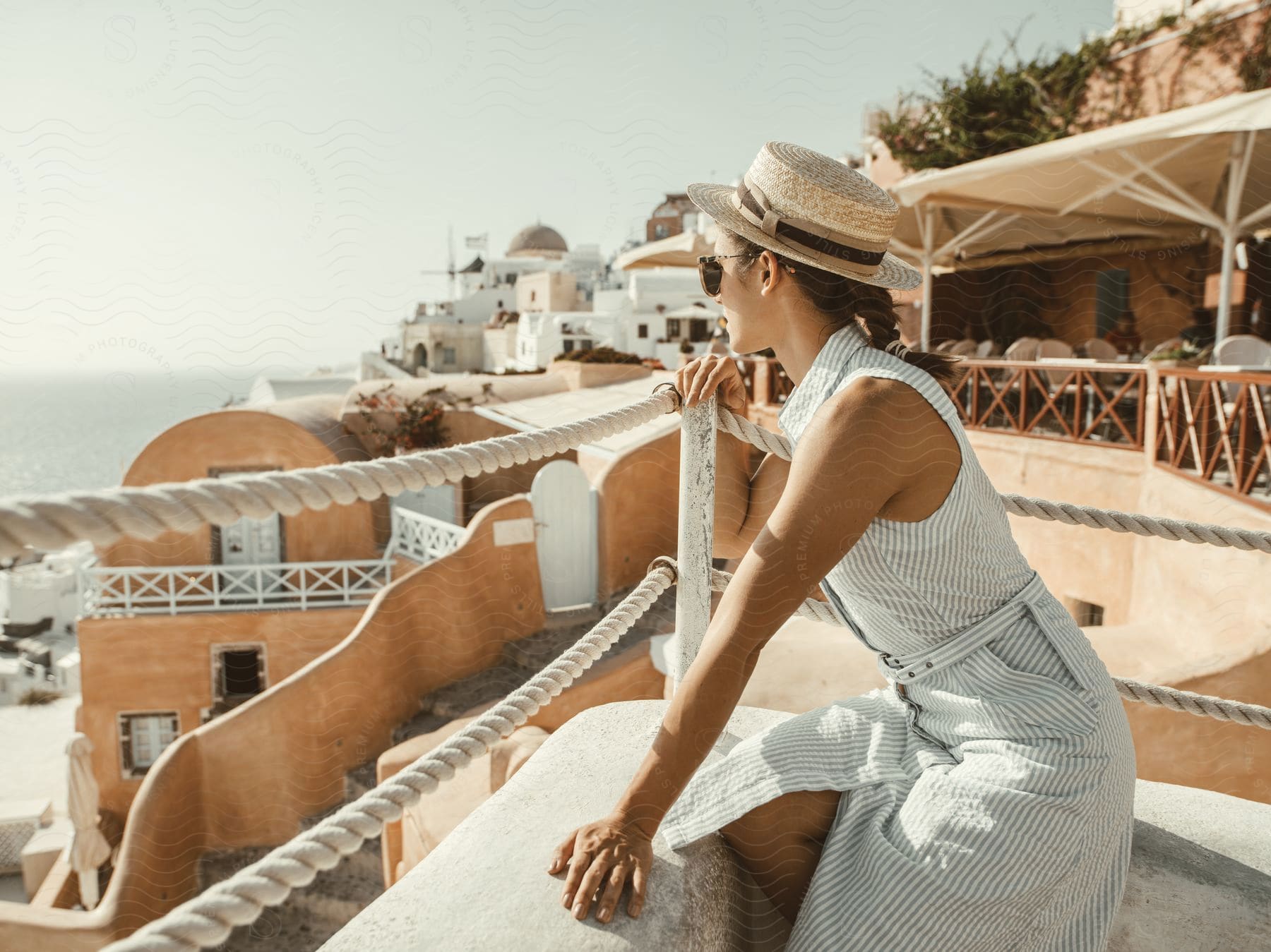 Woman sitting on concrete and watching the sea from a tourist destination with mediterranean houses on a sunny day