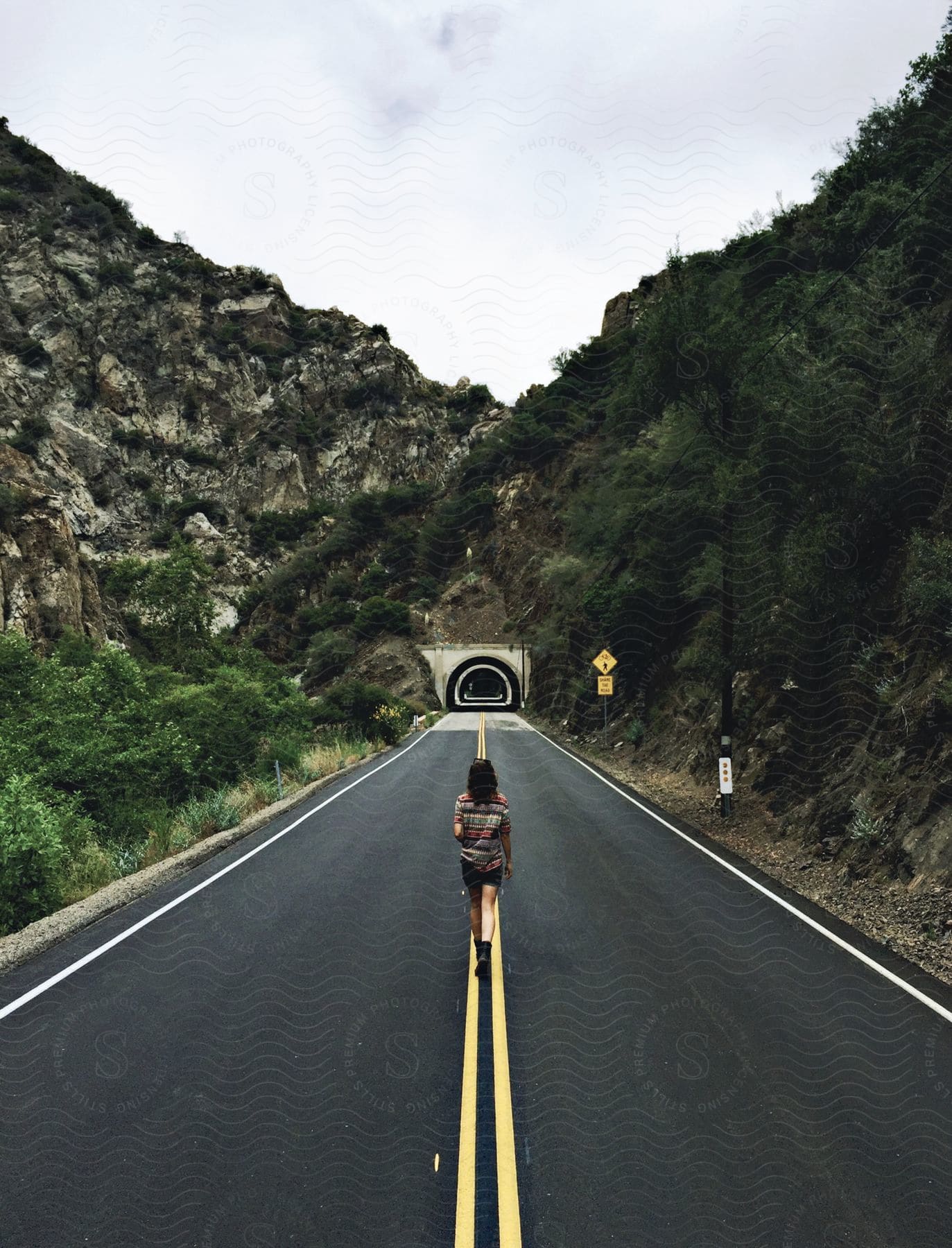 A woman walks on a mountain road towards a tunnel