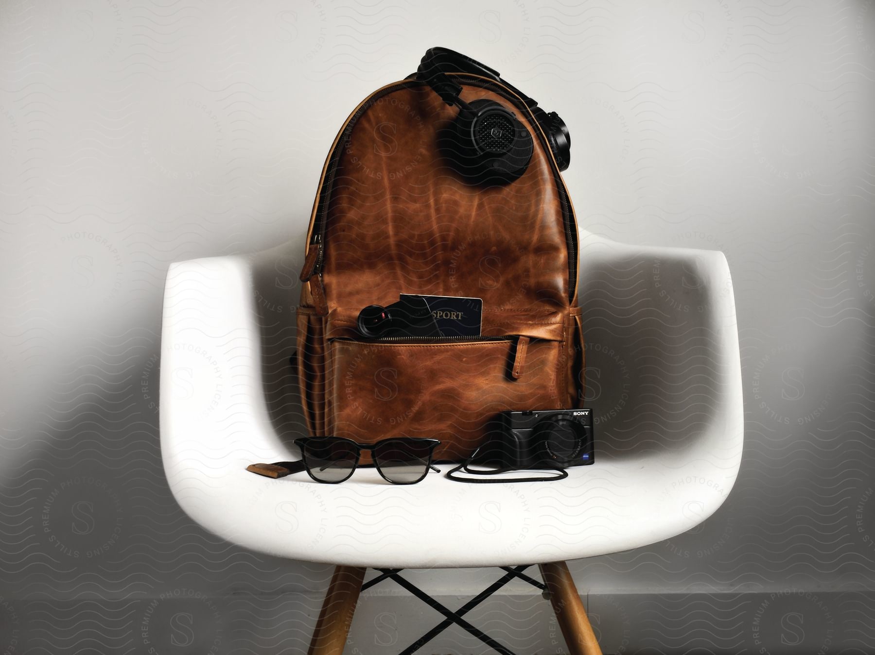 A white chair with a backpack headphones sunglasses and a camera on top