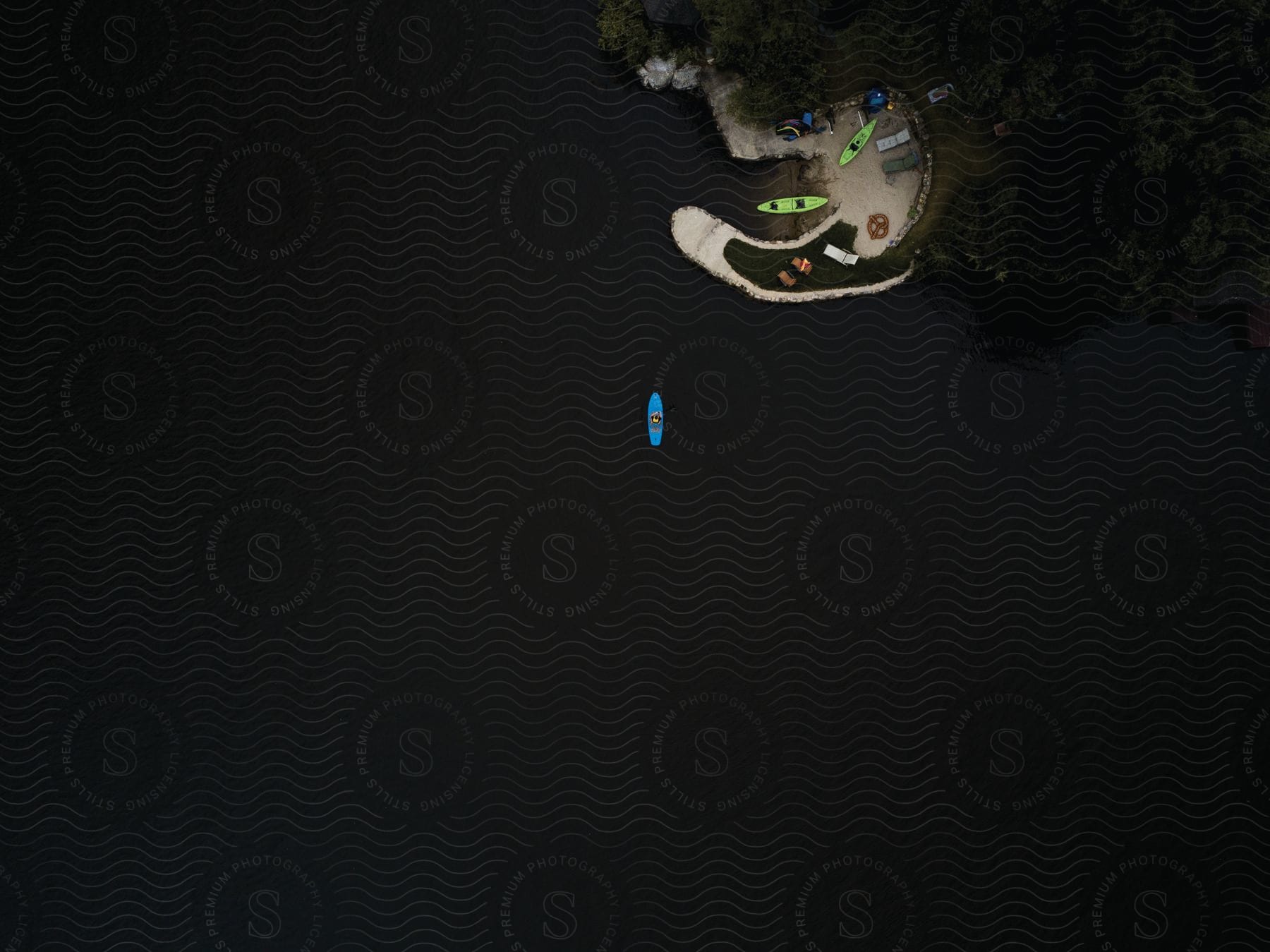 A blue canoe is on the lake with other canoes on the banks