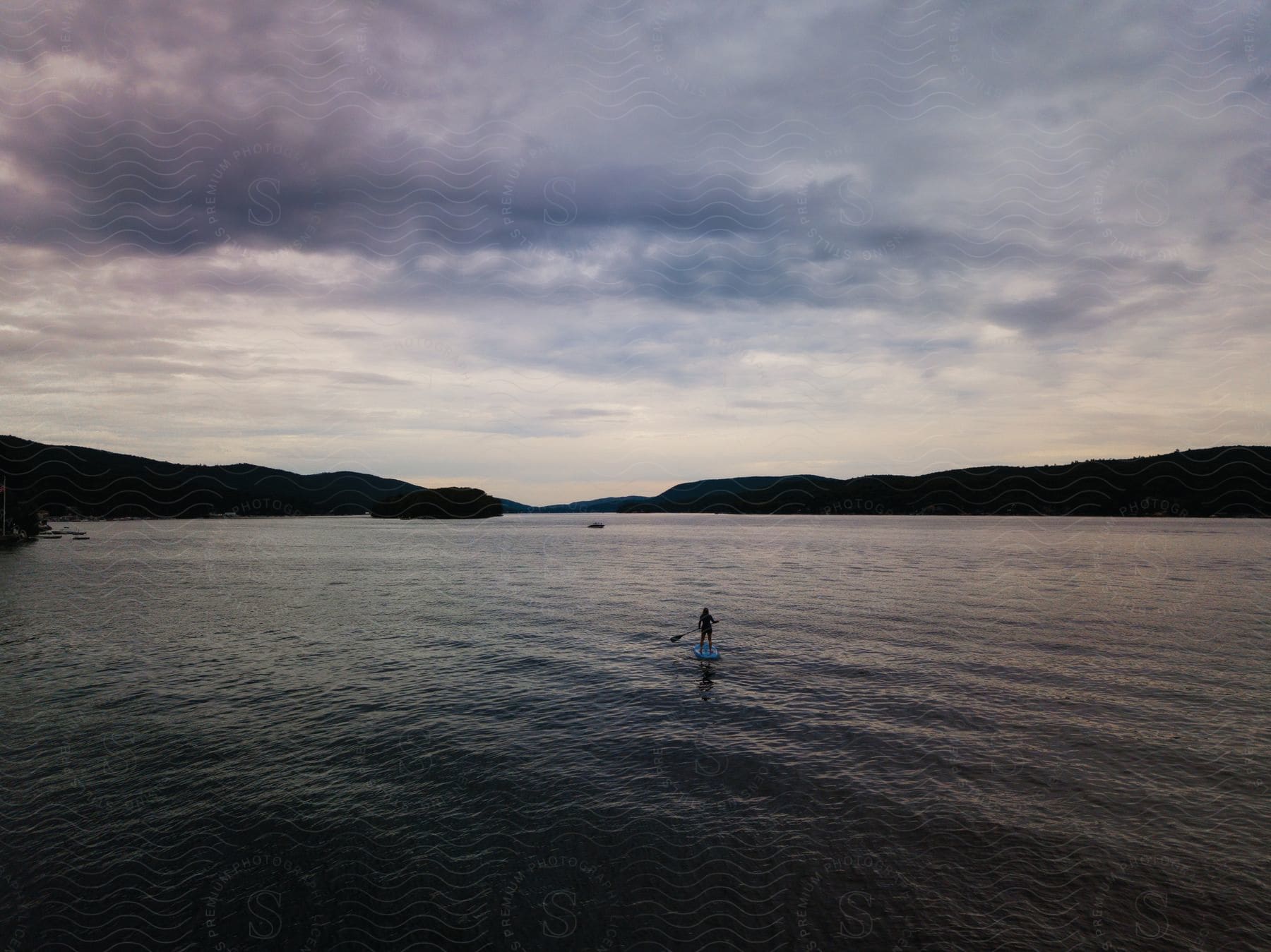 A person standing on a small boat with a paddle in a natural outdoor setting surrounded by a lake water and landscape