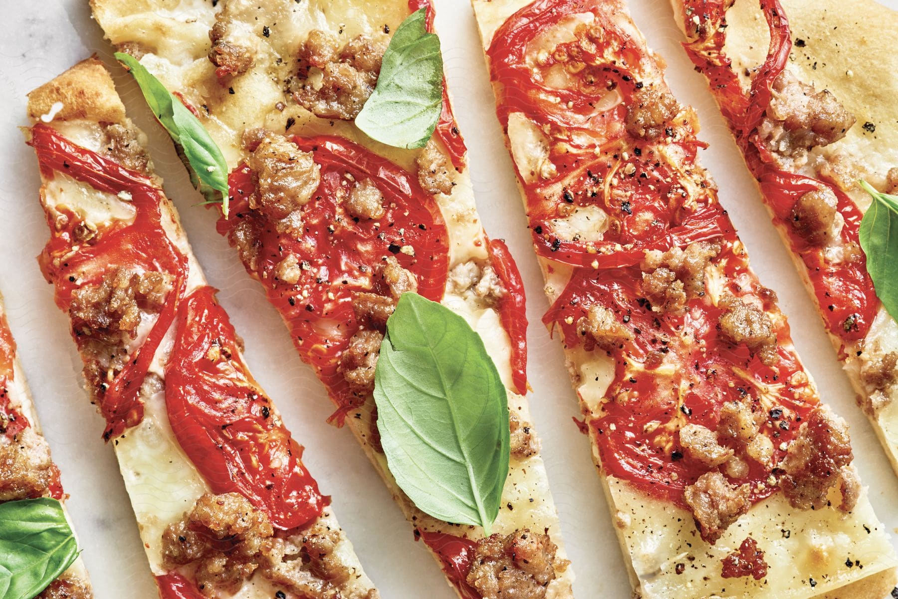 A flatbread pizza with sausage tomatoes and basil