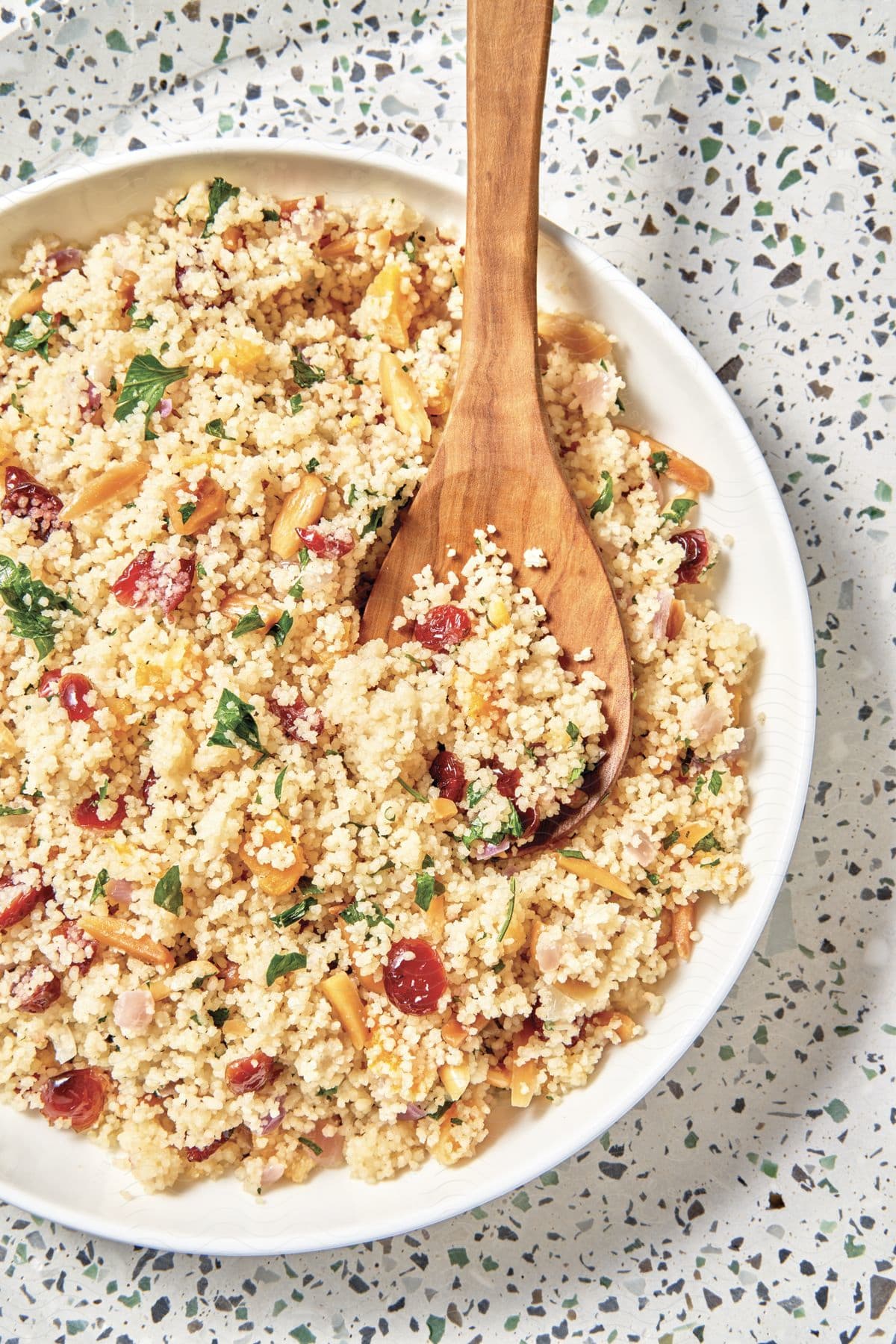 A topdown shot of a dish of couscous with a wooden spoon on it