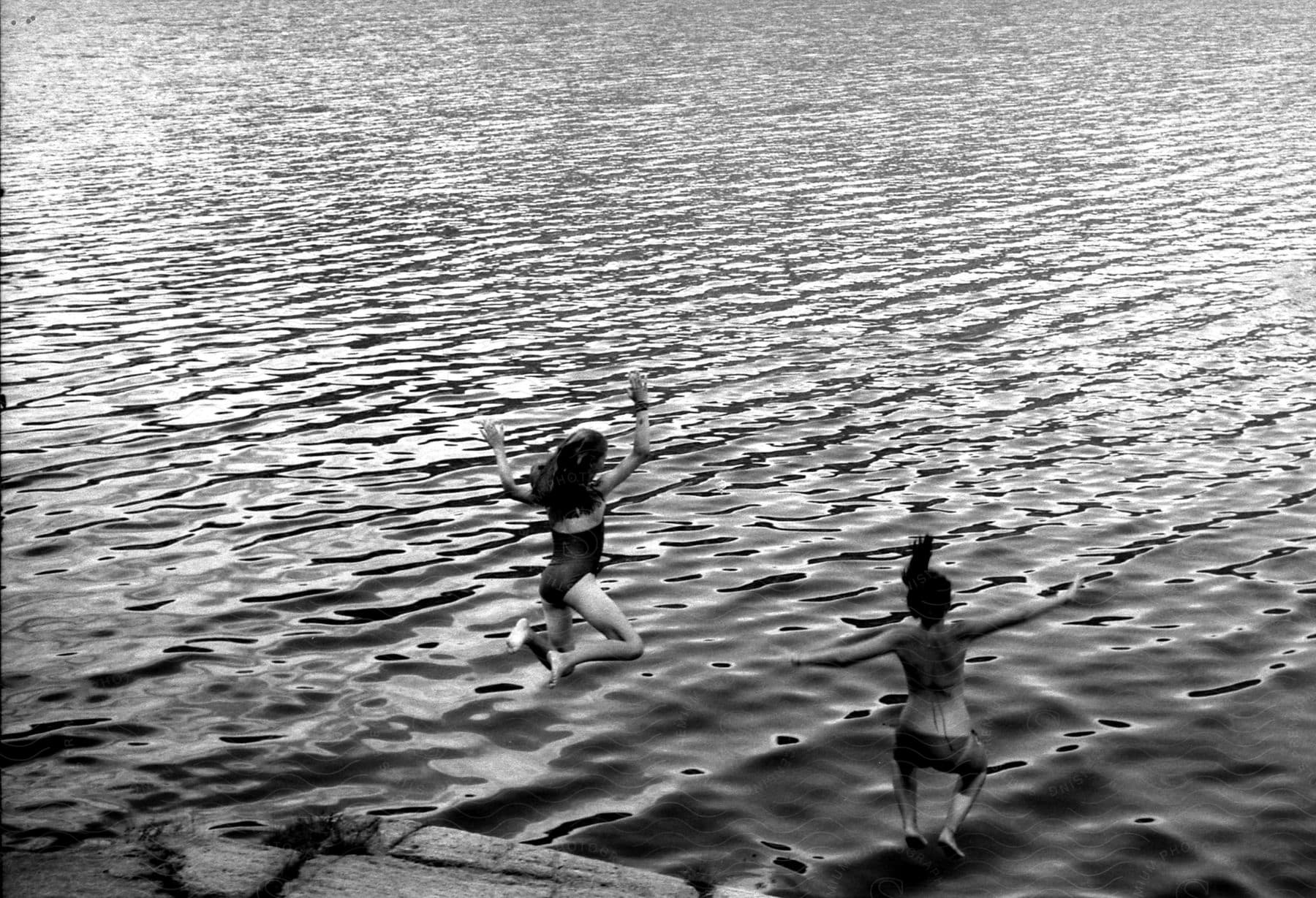 Two girls jumping into the ocean during the day