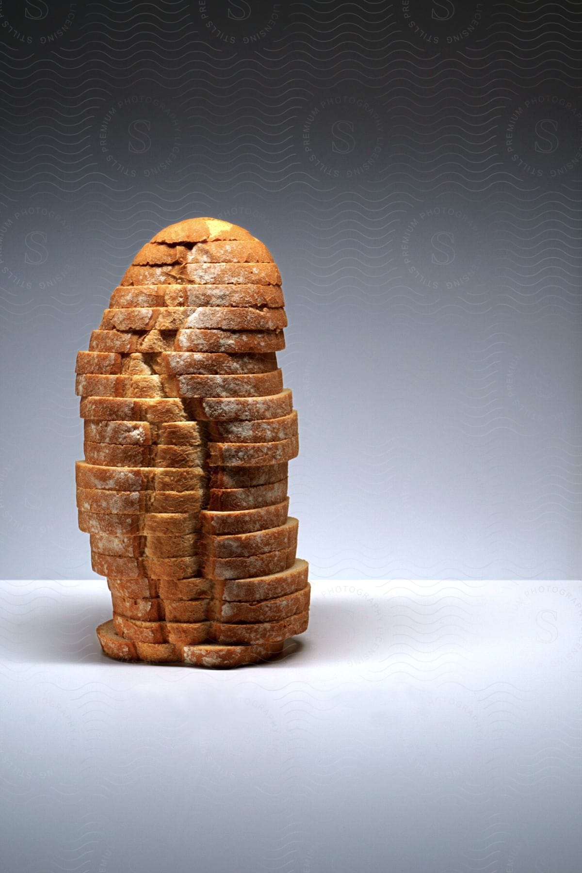 A sliced loaf of bread is presented vertically in a studio environment on a grey background