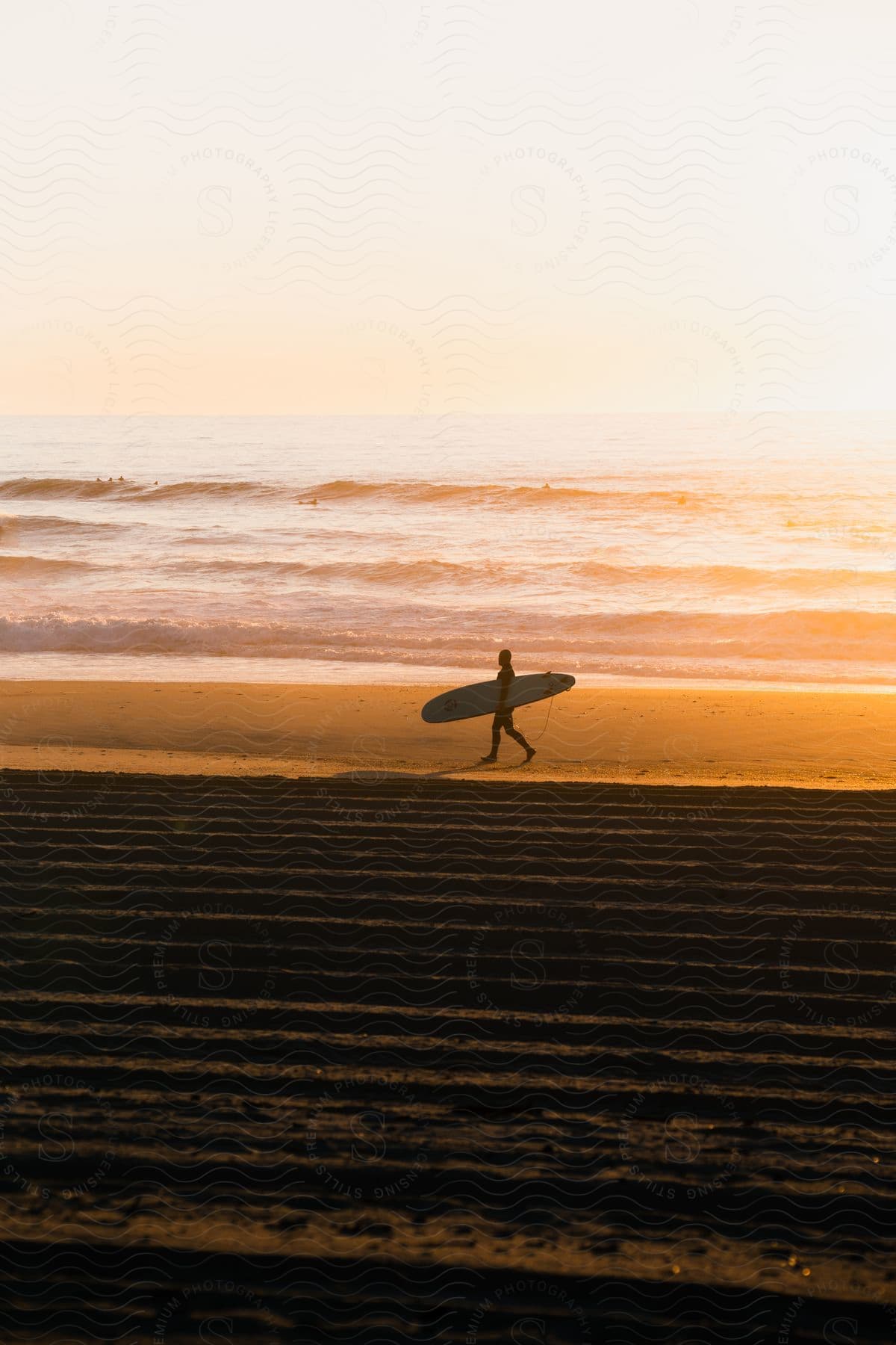 A person walking along the beach with a surfboard under his arm