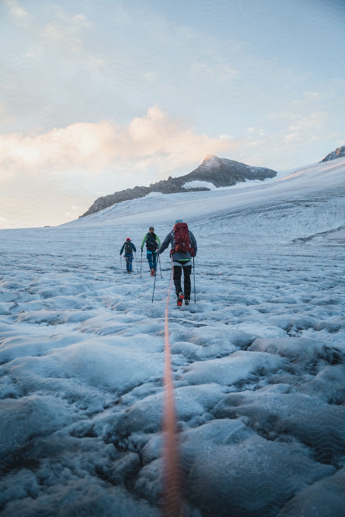 Three people trek across an icy landscape toward mountains following a rope