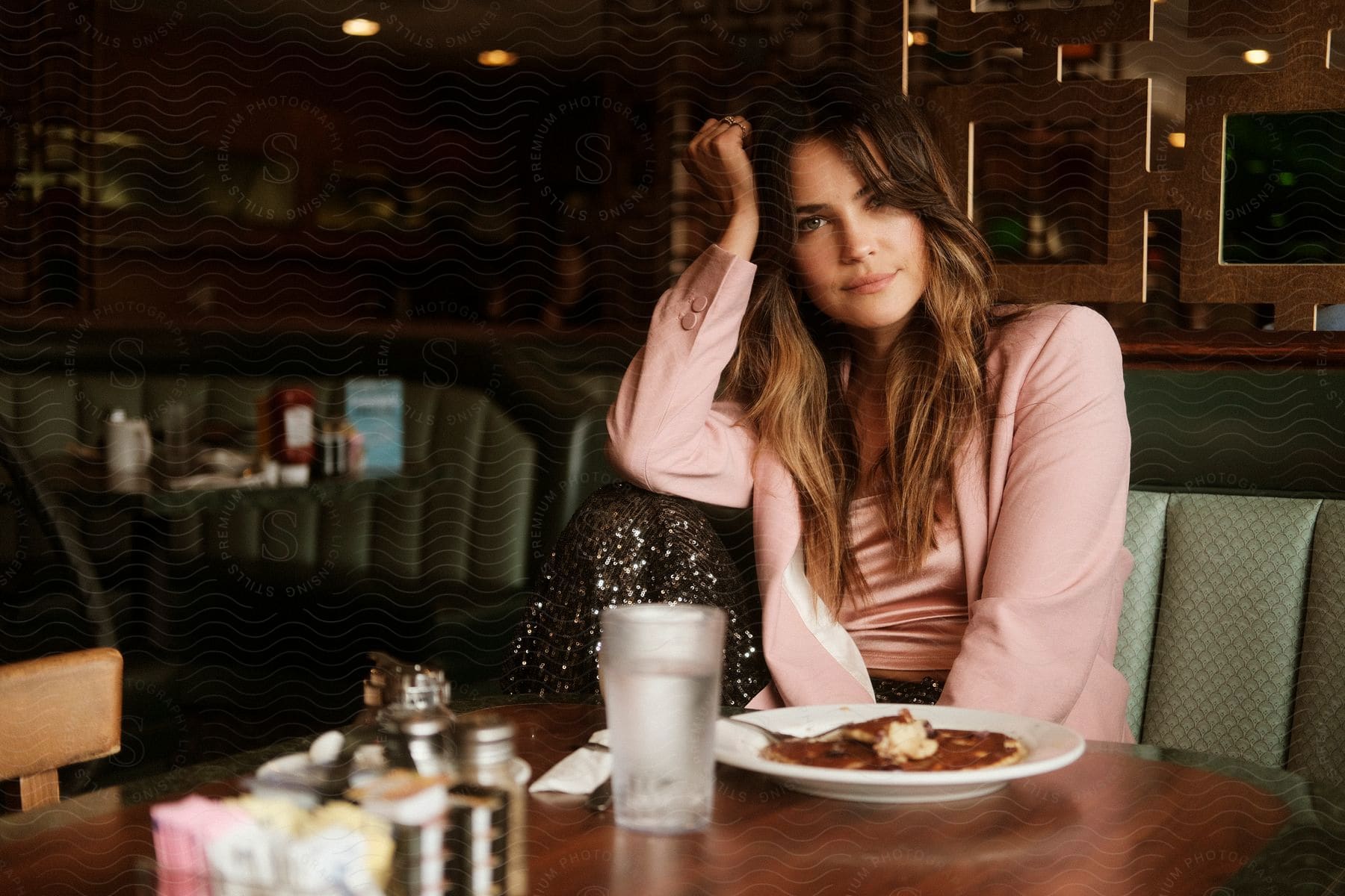 A woman with brown hair wearing a pink blazer jacket and shirt sits at a table and poses for the camera at a cafeteria