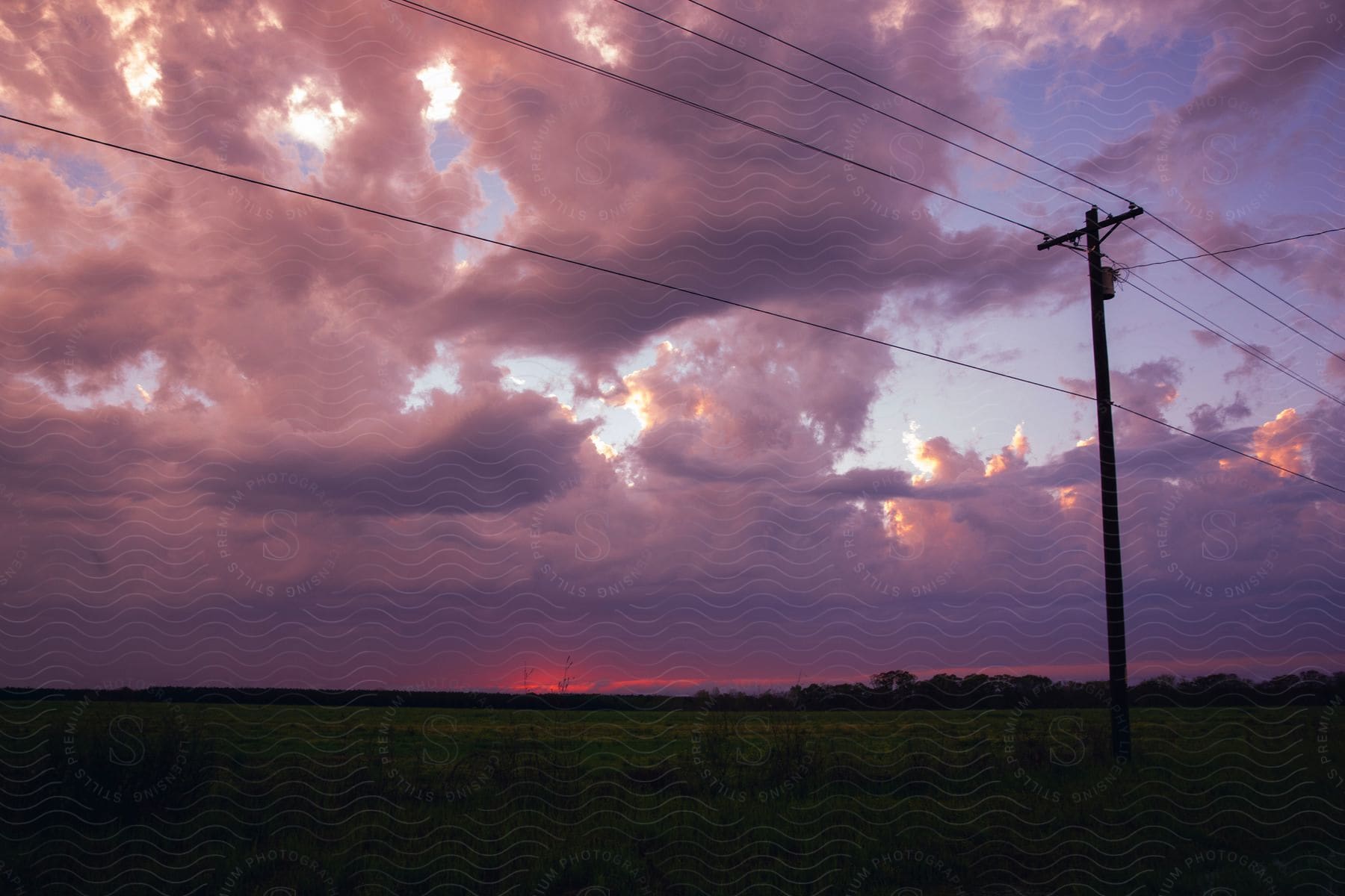 Landscape of utility pole with cables against the clouds floating in the sky at sunset