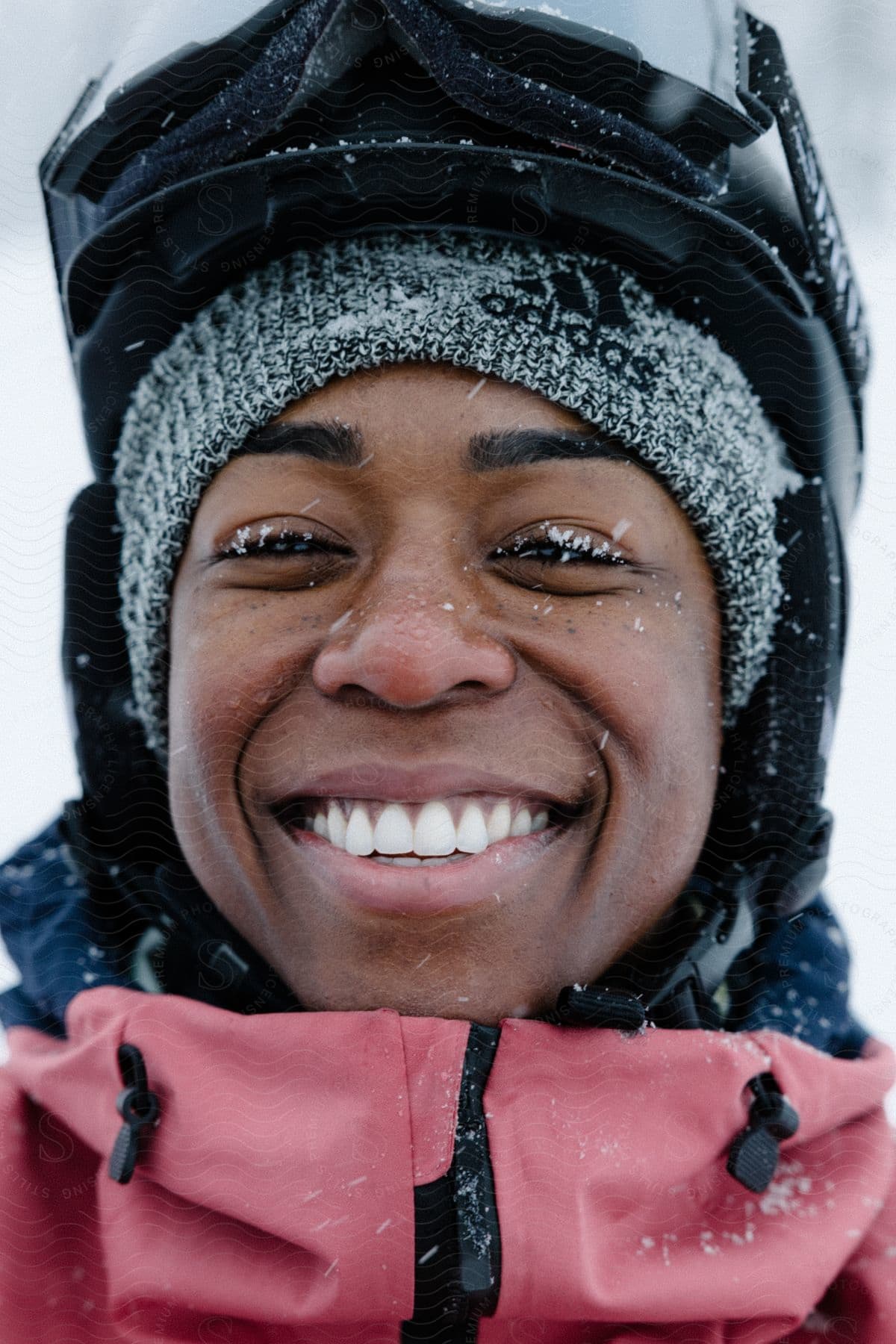 Portrait of a woman wearing coats, a beanie, and snow goggles, smiling.