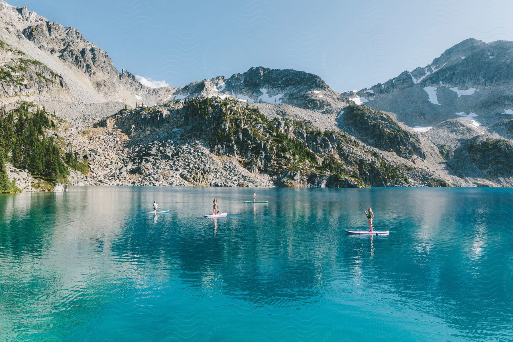 Friends paddle boarding on a clear blue lake in the mountains with glaciers in the distance