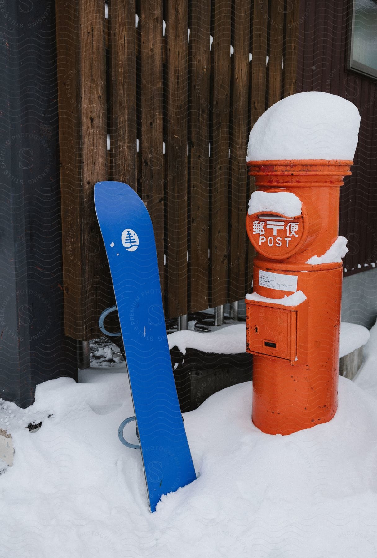 A red post box stands in a snowy landscape with a weathered blue board nearby