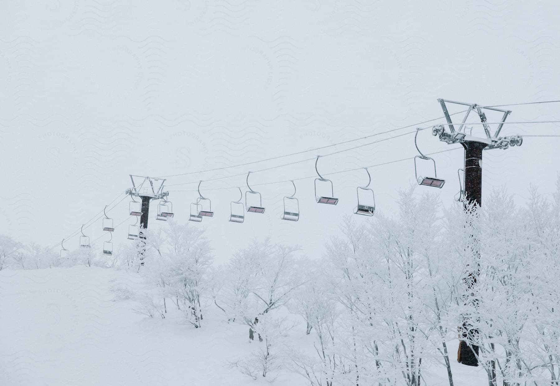 Empty ski lift seats hang from cables over snowcovered trees on the mountainside