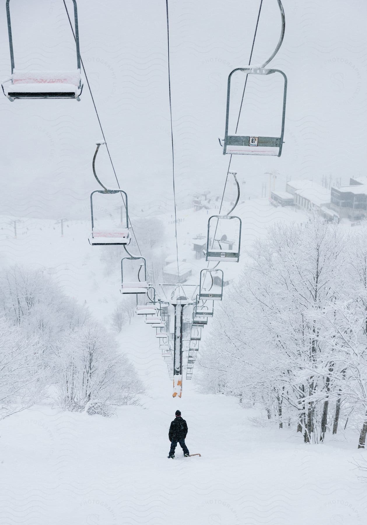 A snowboarder stands beneath a ski lift on a snowy ski slope