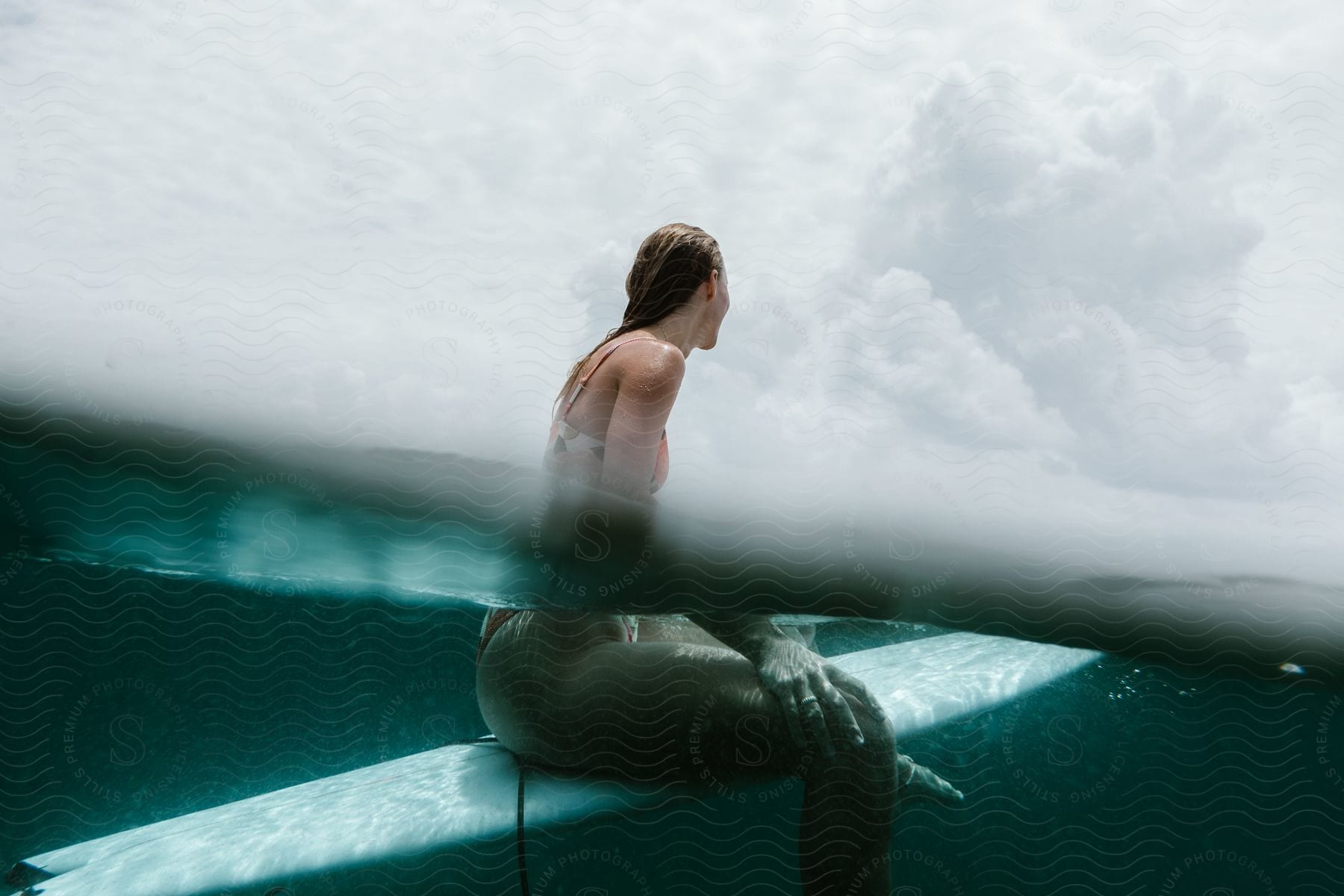 A woman sitting on a white surfboard in the ocean looking at a cloudy sky