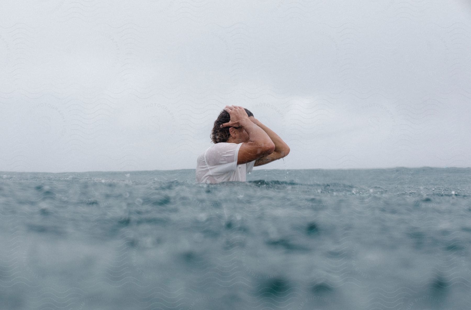 A man stands in the ocean with his hands on his head