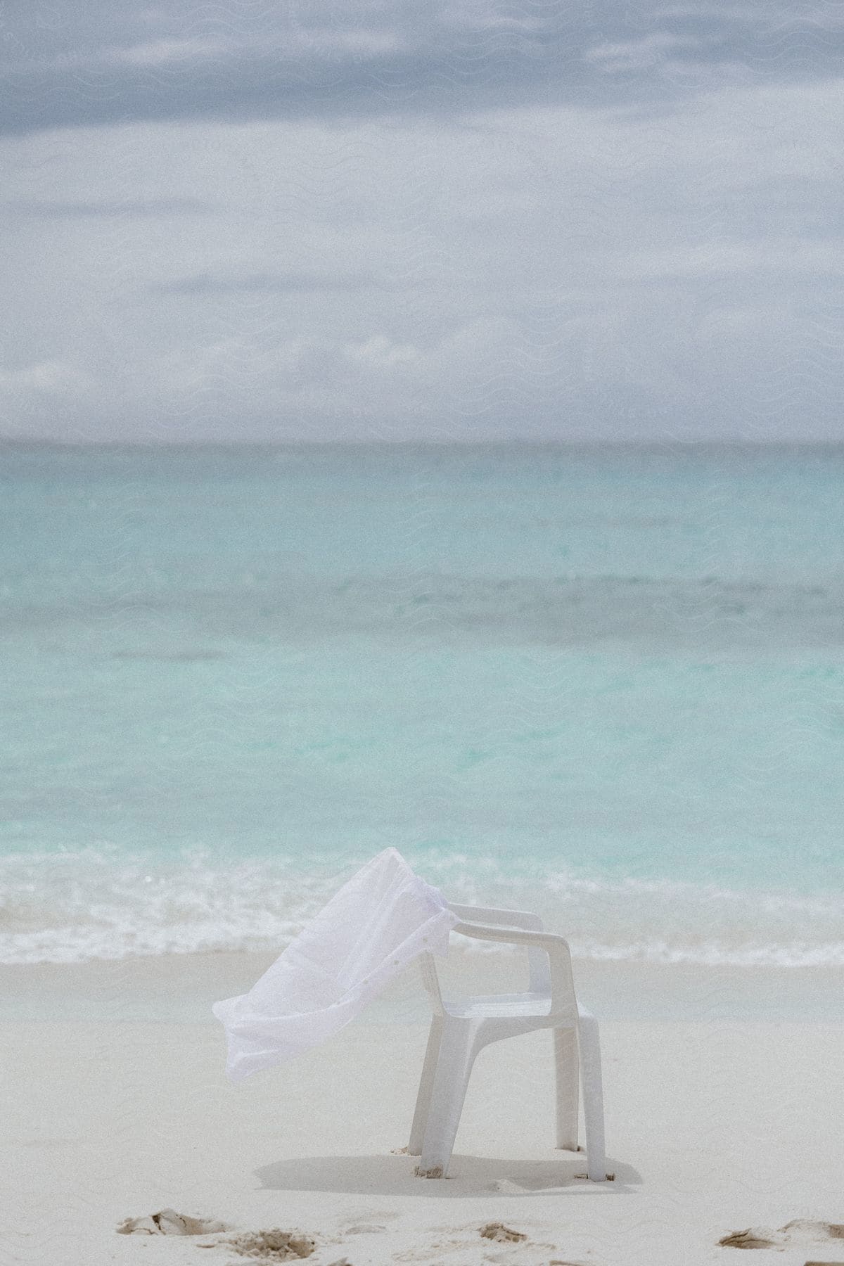 A white shirt hanging from a plastic garden chair on a beach with the ocean in the background