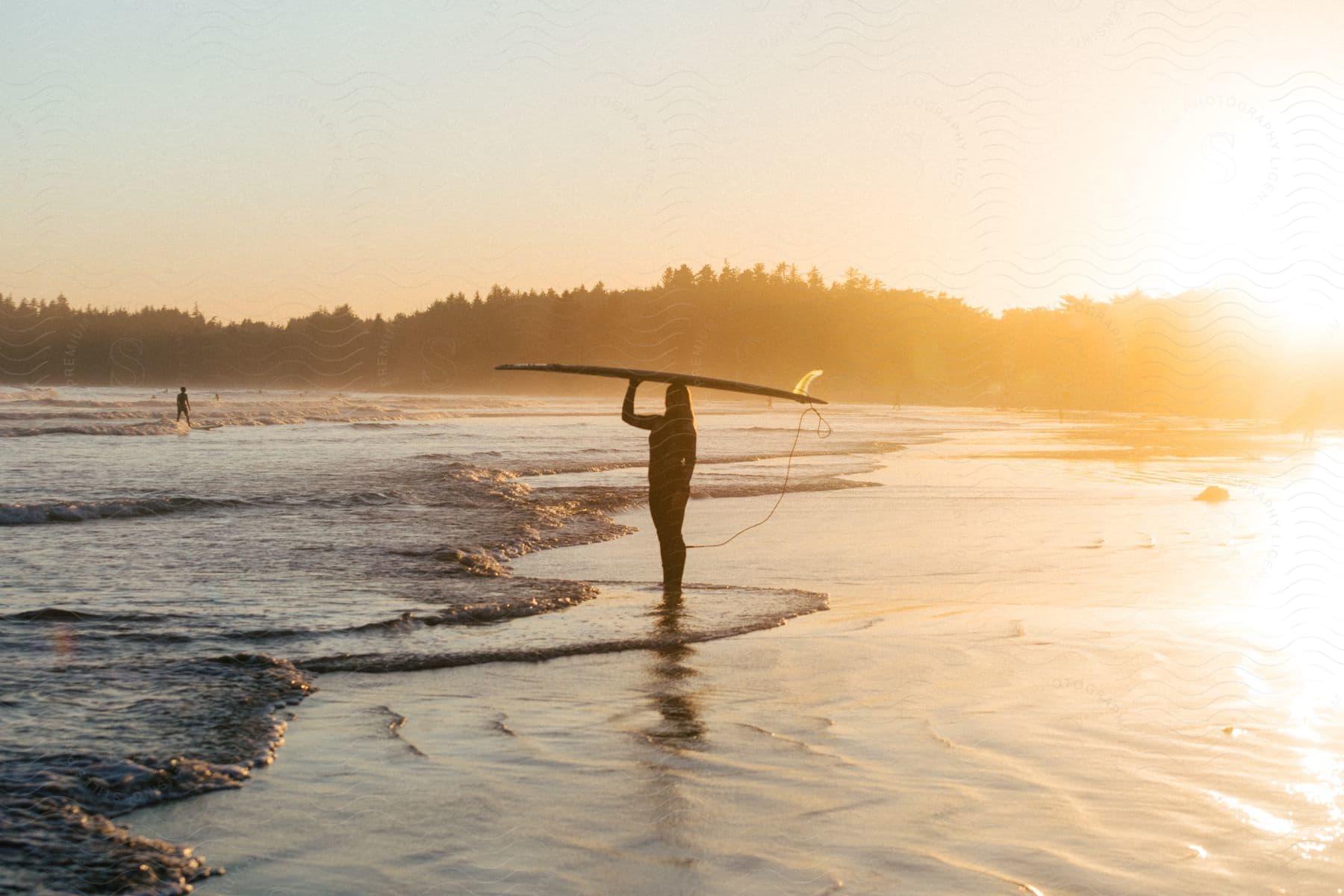 A woman holds a surfboard on her head while standing on a sunny beach