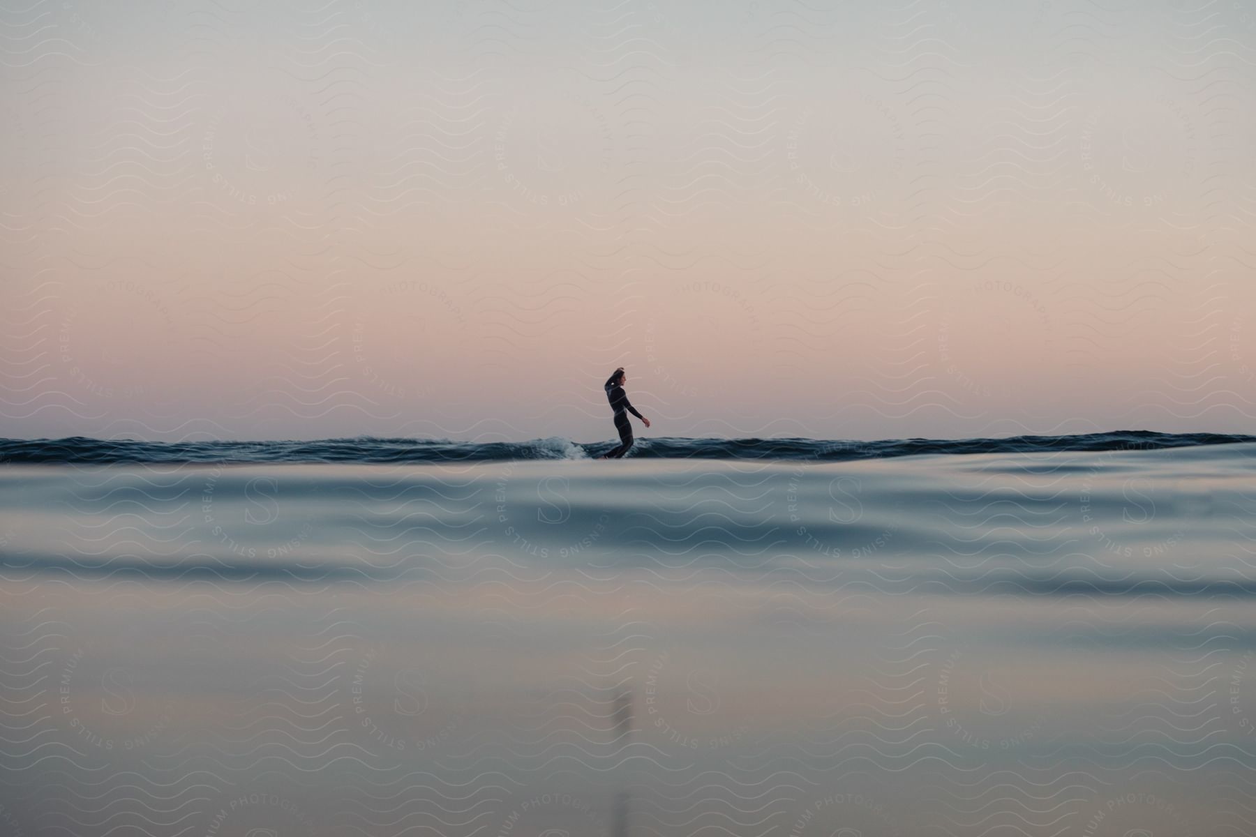 A woman is surfing in the ocean at dusk or dawn