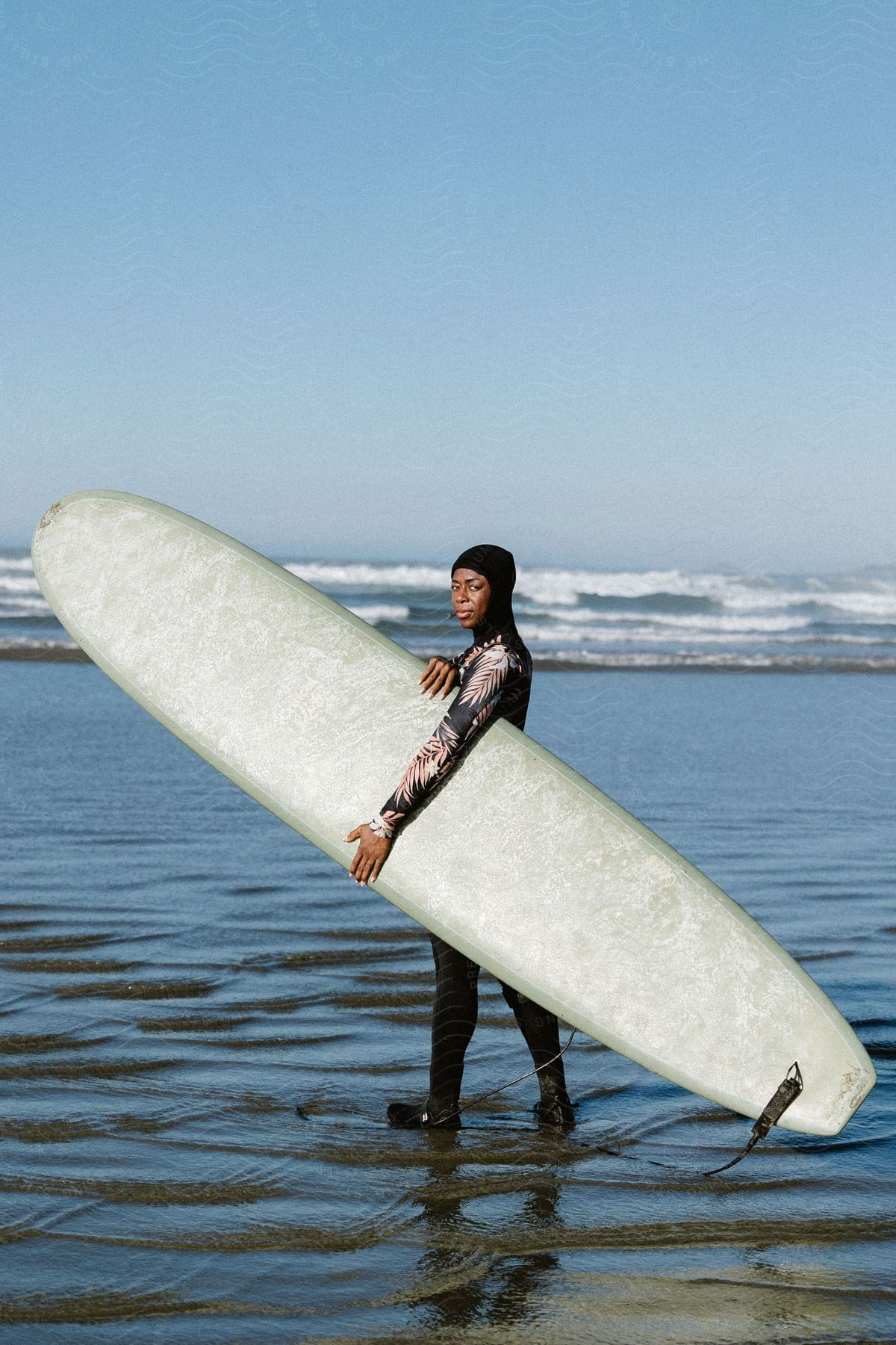 A woman wearing a wet suit is holding a surfboard on the beach.