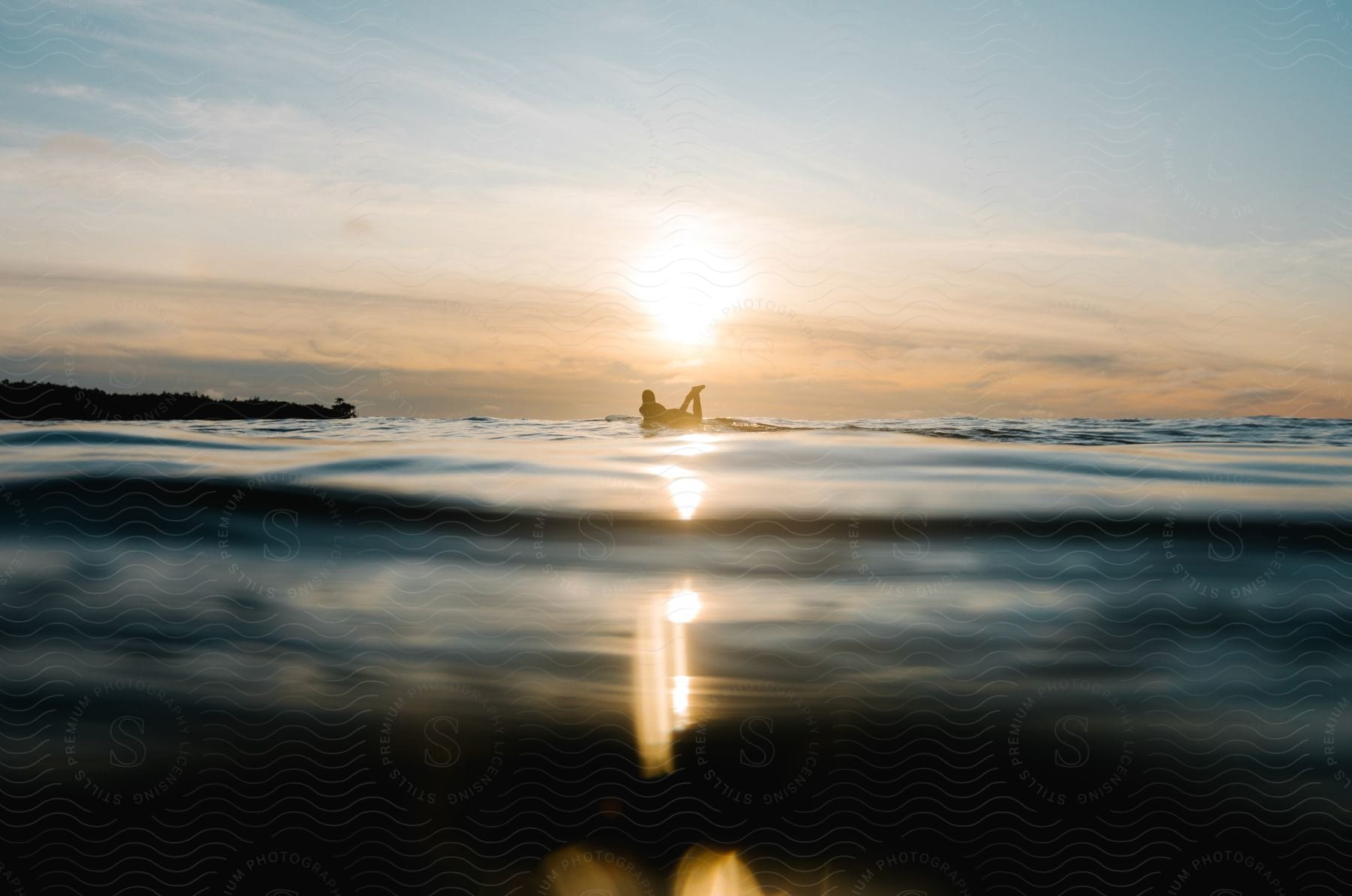 A person paddling on a surfboard against the setting sun on a calm ocean