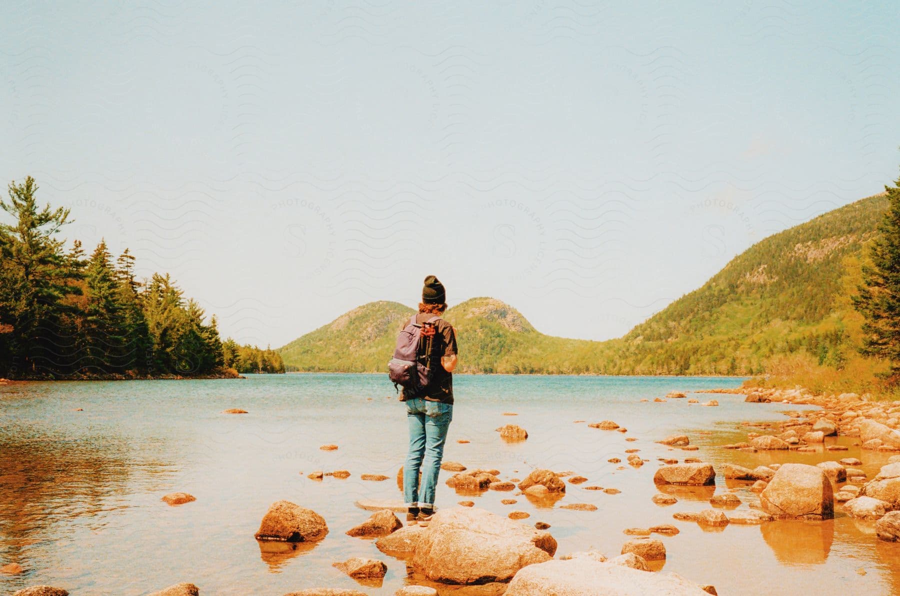 A young adult stands in nature near a lake carrying a backpack