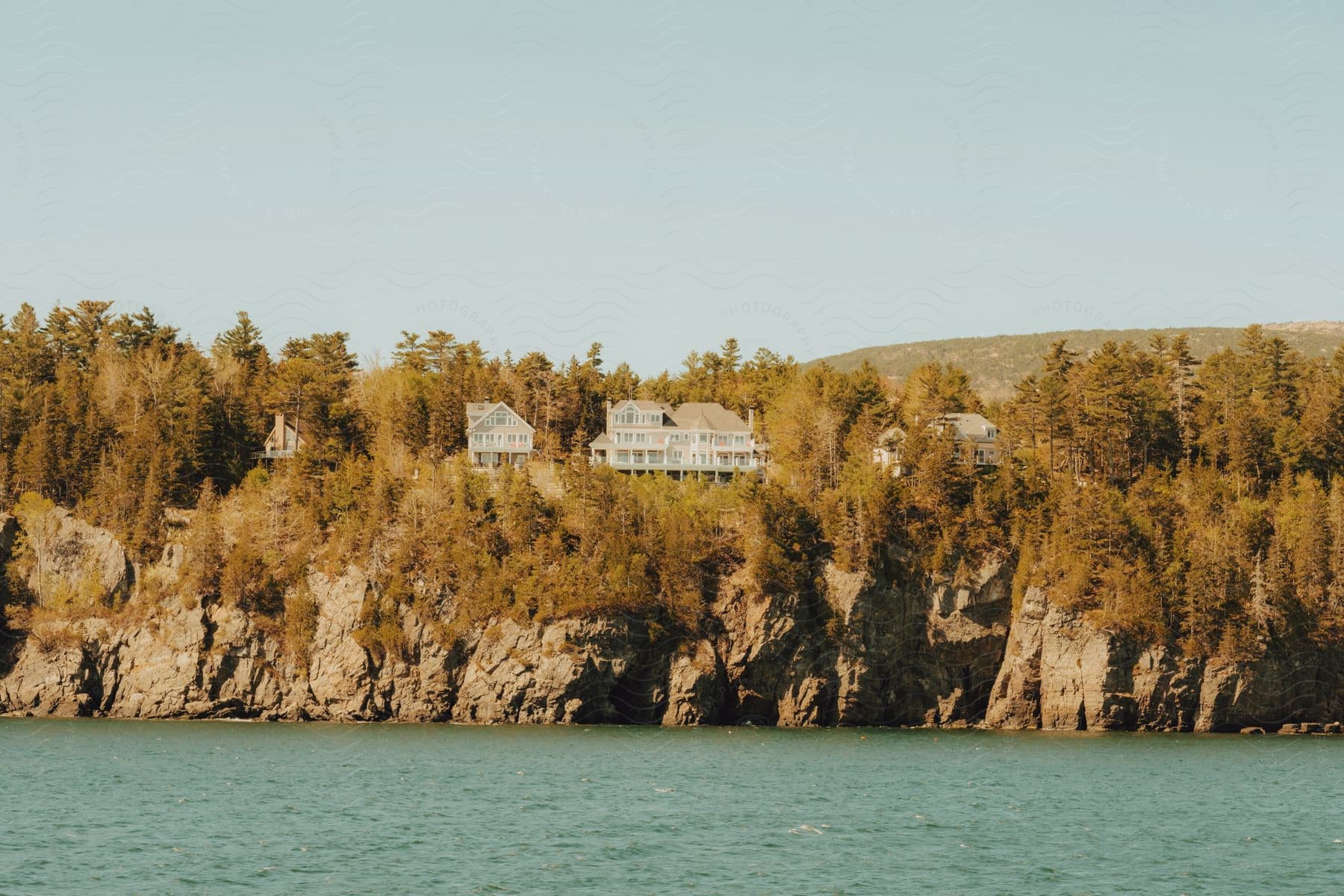 Several homes on a forested cliff overlook a lake