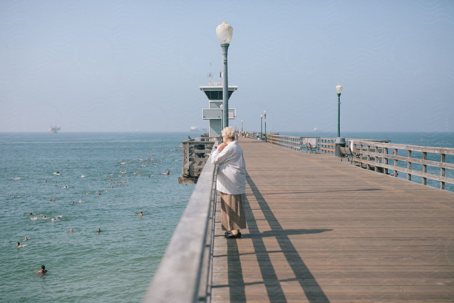 A woman stands on a pier looking out at ducks on the ocean