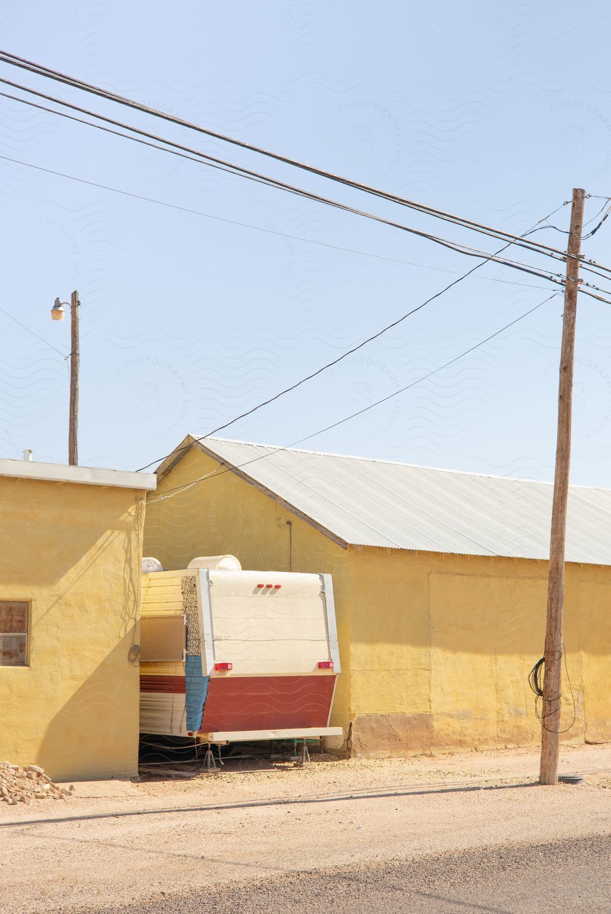 An rv or trailer is parked between a yellow house and a secondary building