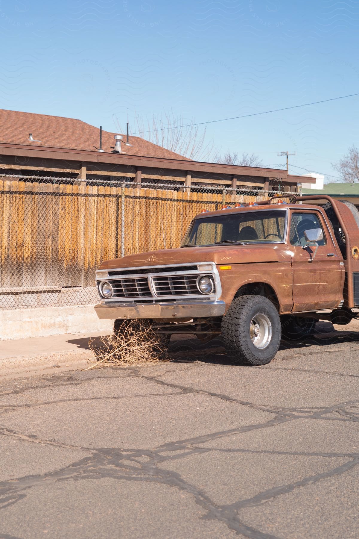 An Old Pickup Truck Parked Next To A Wooden Fence And A Tumbleweedstrewn House On A Dusty Road In The Midday Sun