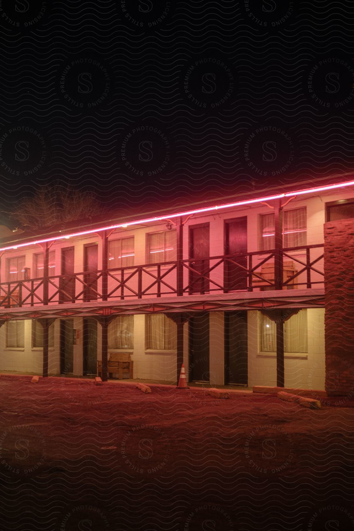 A two level motel with outside room entrance doors empty parking spaces and a red light above the second level balcony walkway at night