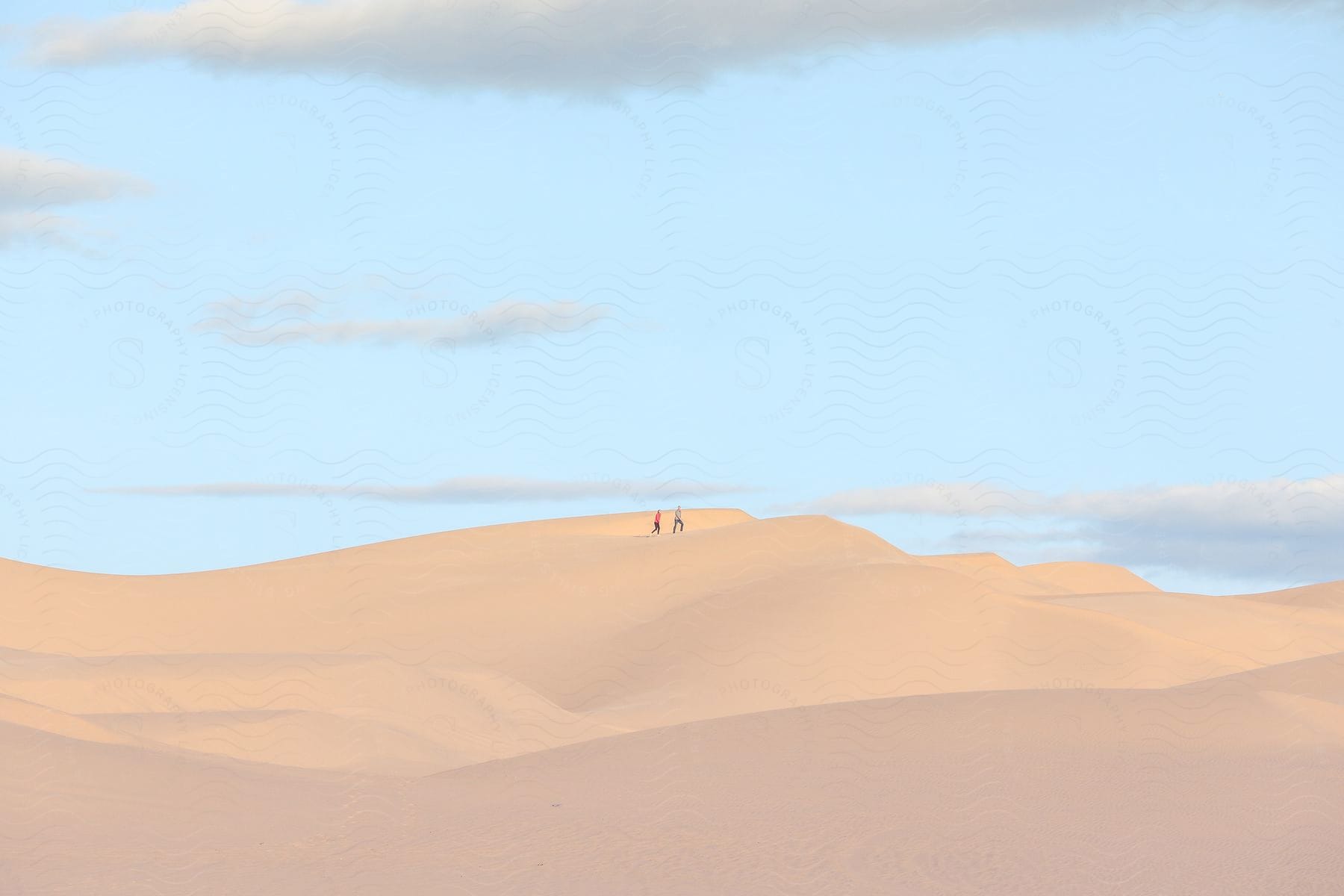 Two people walking on sand dunes in the desert during the day