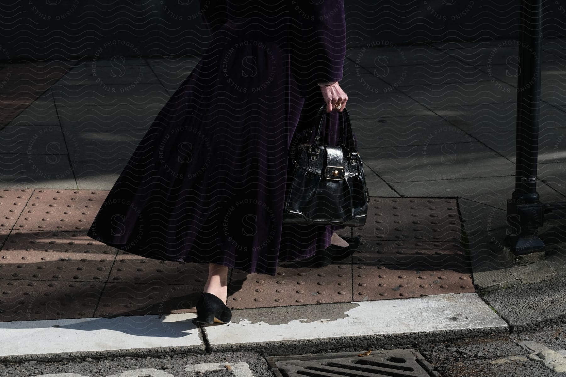 A woman walking on a grey road surface carrying a handbag and wearing high heels