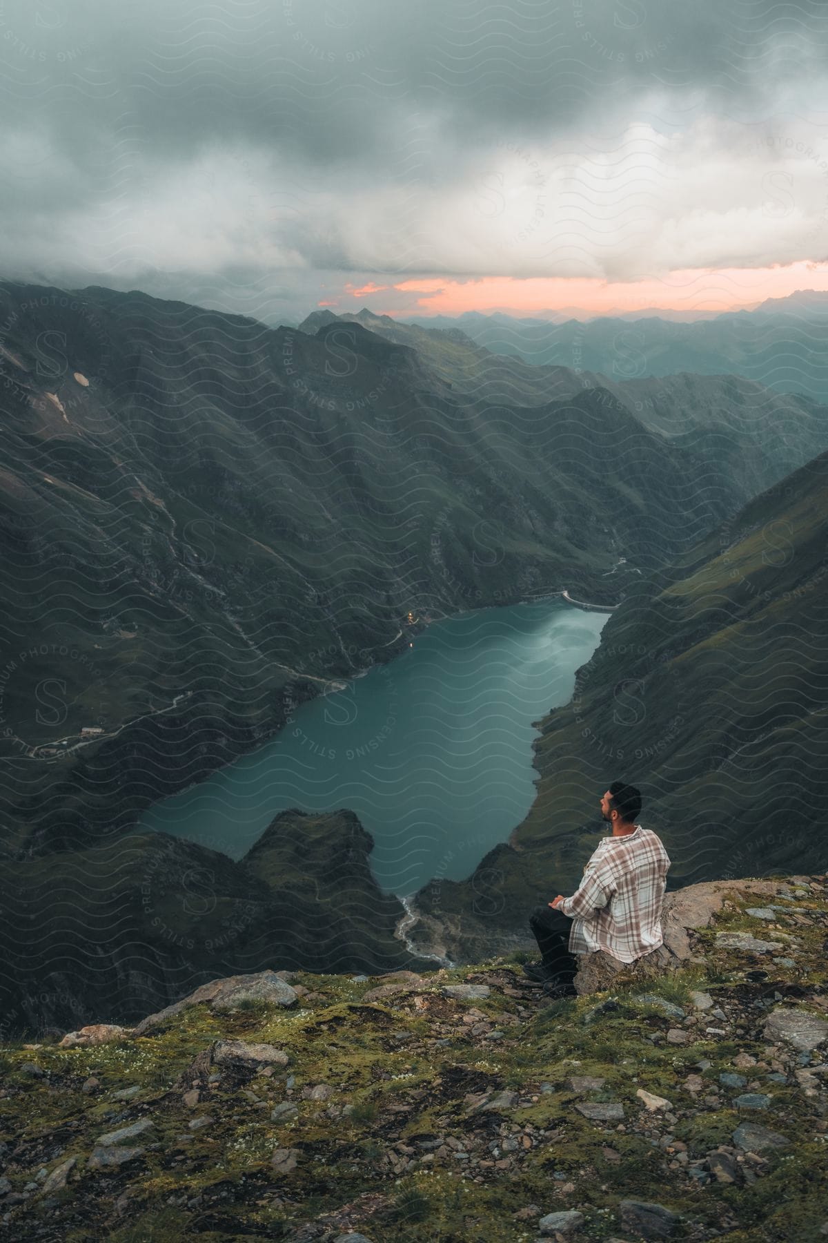 A man sitting on the edge of a cliff overlooking a lake and mountains